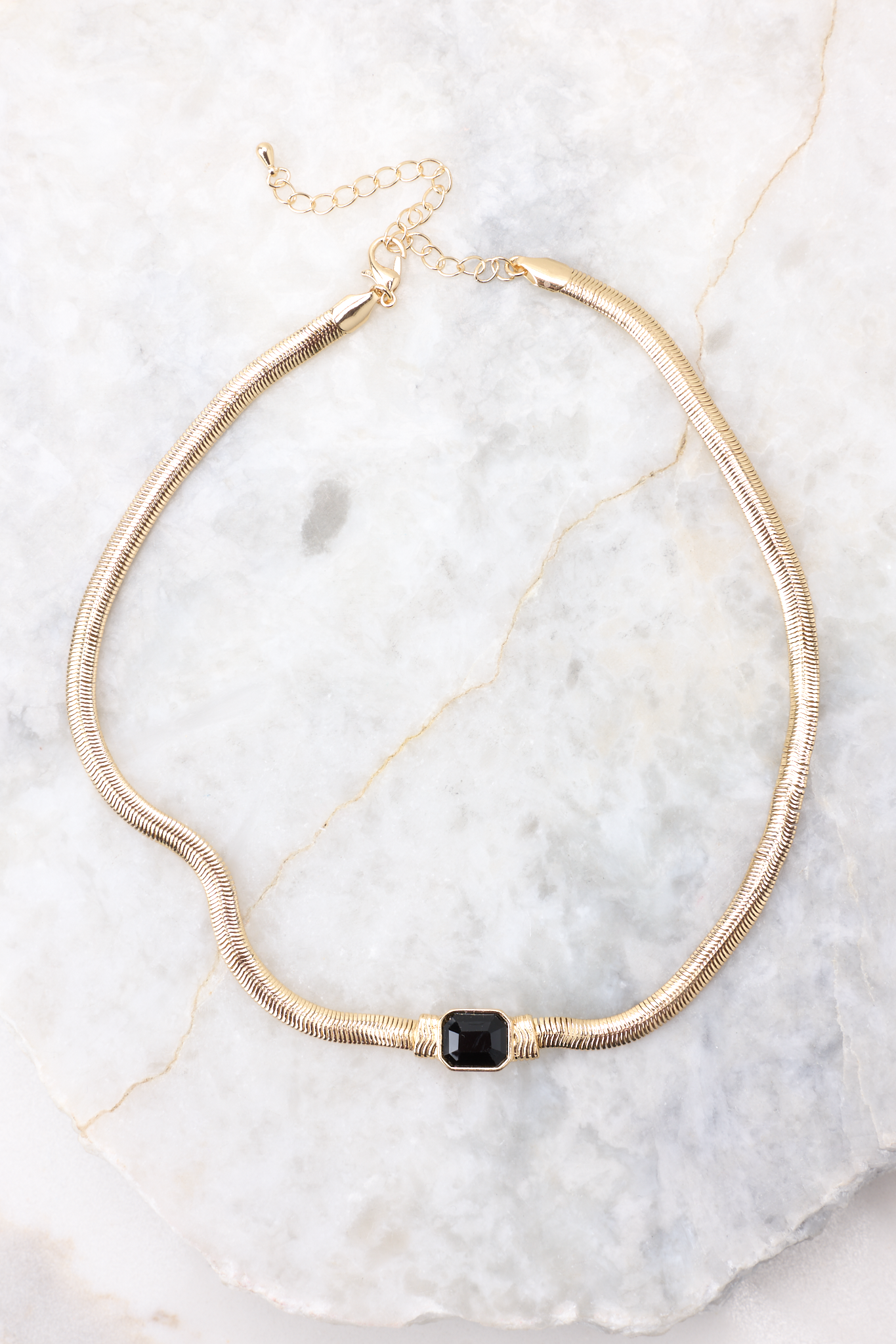 Overhead marble shot of necklace that features a gold snake chain, rhinestone detailing, and a lobster clasp closure.