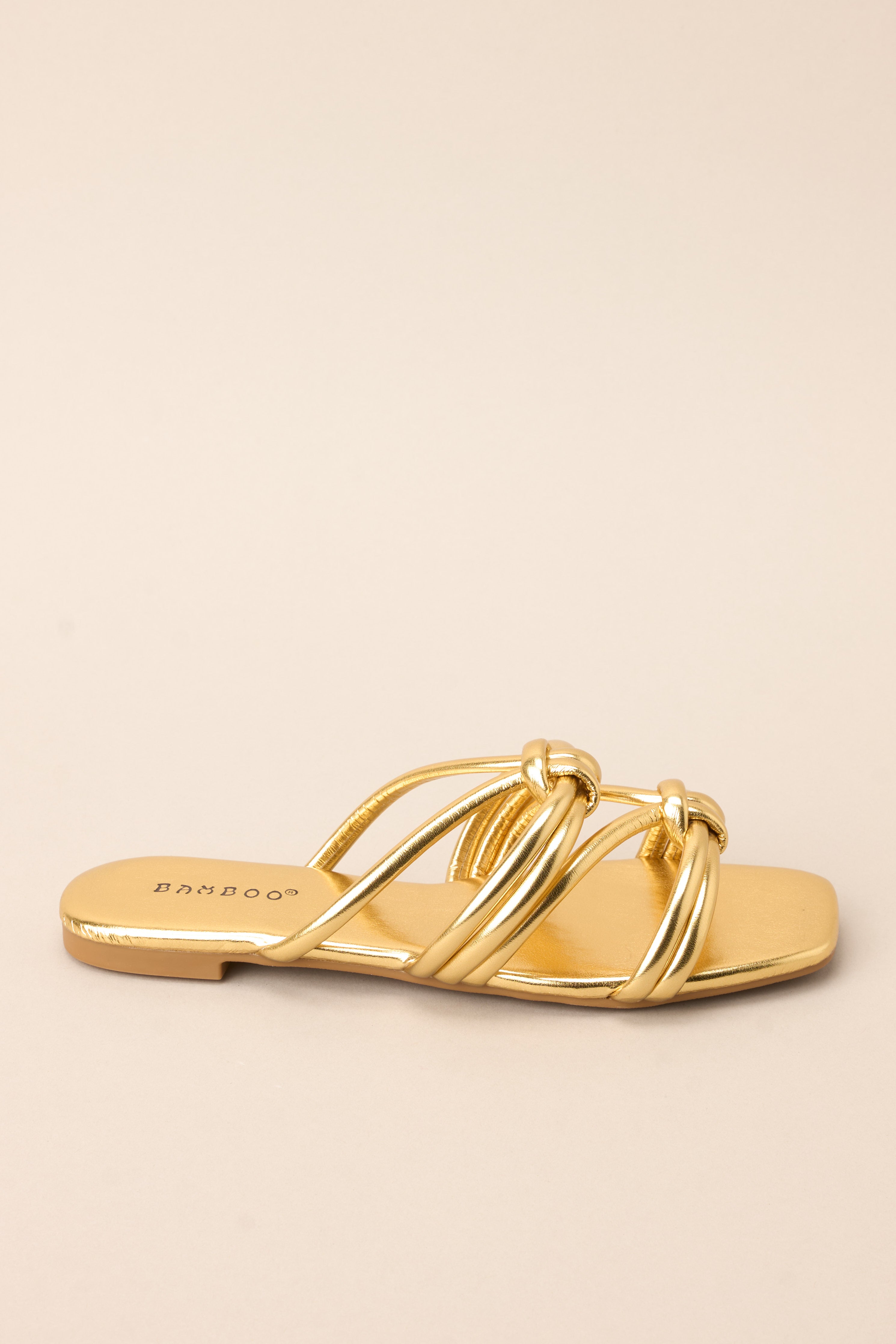 Outer side view of these gold sandals that feature gold knotted straps, and a slip on design.