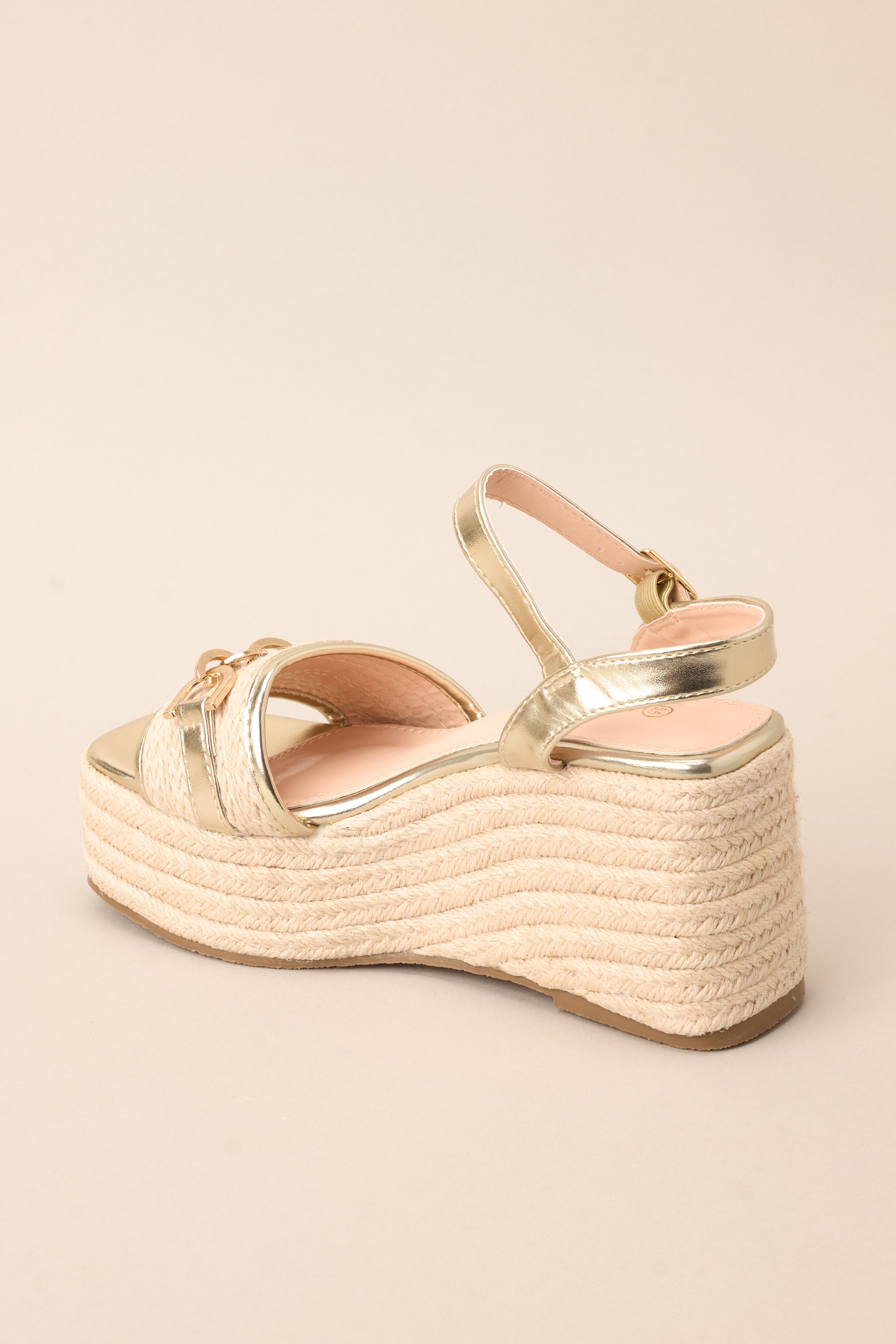 Inner-side view of these sandals that feature gold hardware, straps across the top of the foot and around the ankles, gold link detailing, and an elevated height.