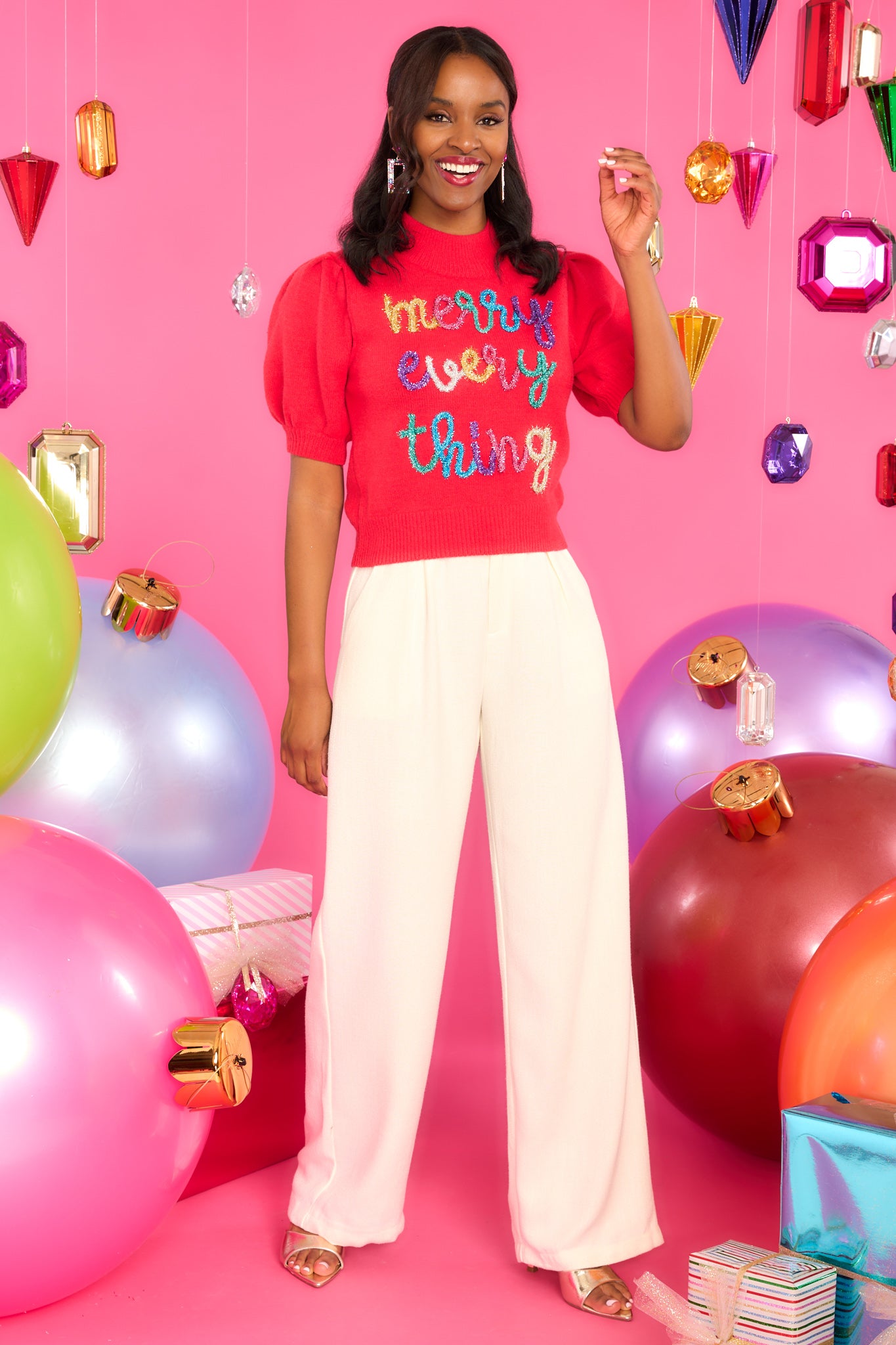 This red sweater features a slight turtle-neck, short puff sleeves with ribbed cuffs, a ribbed hem, and multi-colored tinsel script. 