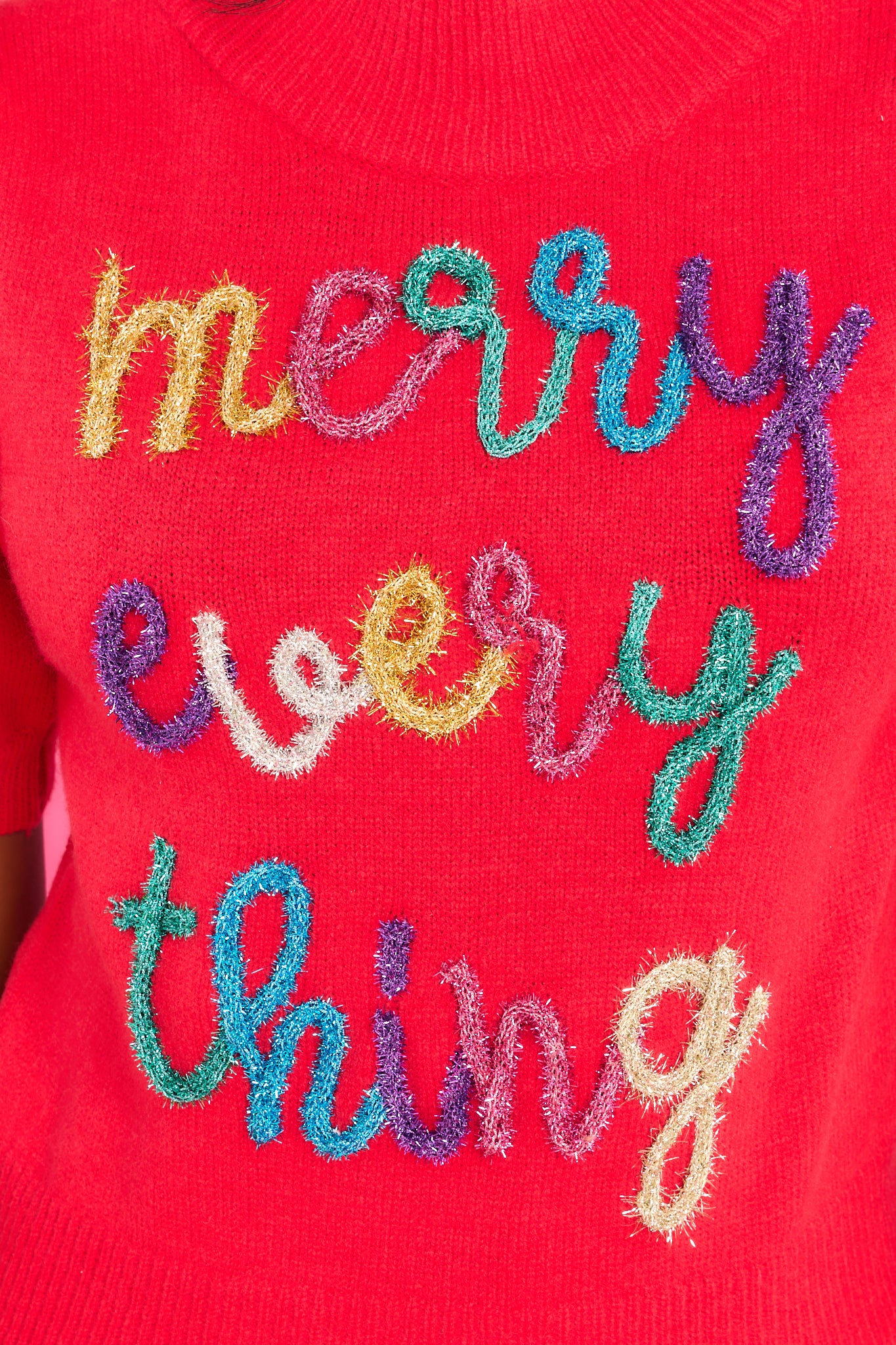 Close up view of this sweater that showcases multi-colored tinsel script that says "merry every thing".. 