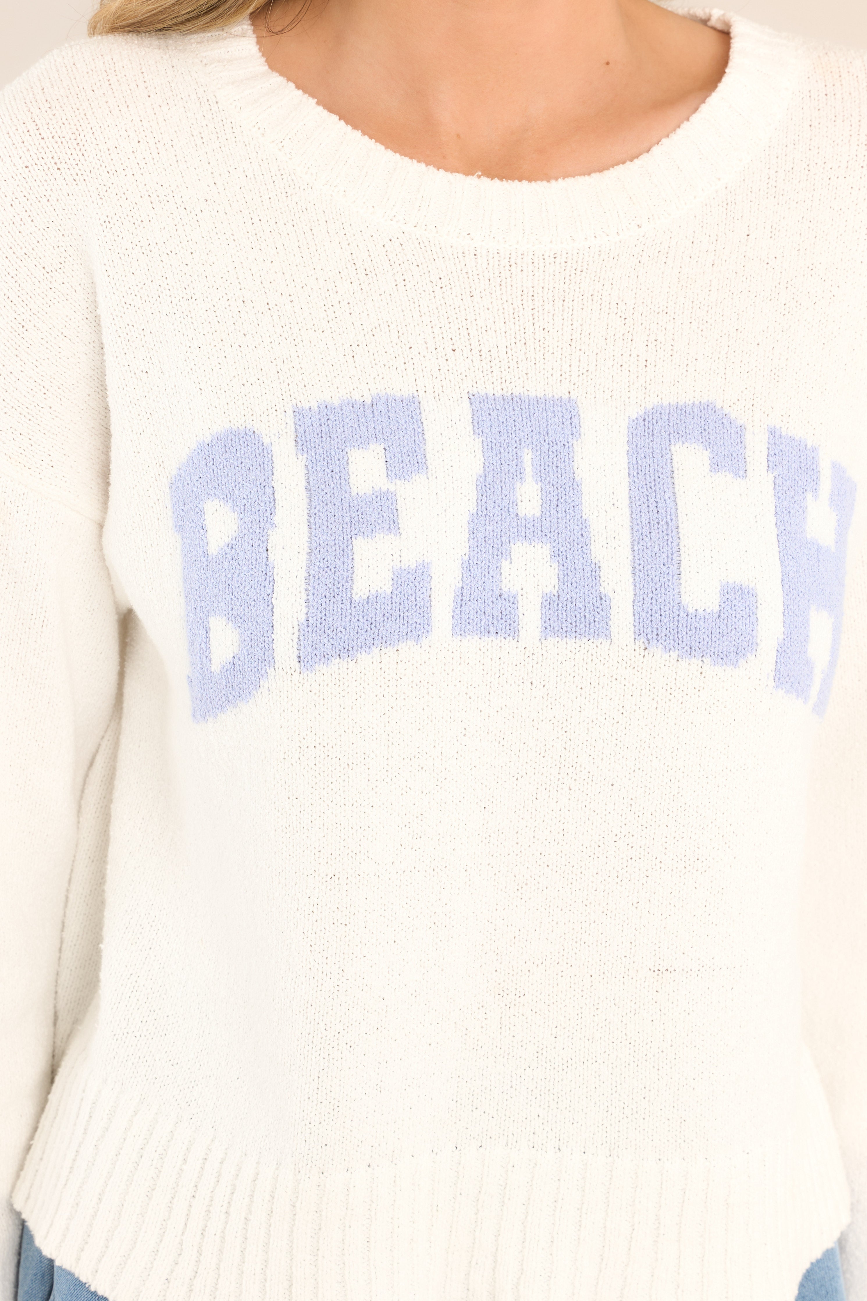 Close up view of this sweater that features a ribbed crew neckline, varsity style wording across the chest, and ribbed cuffed long sleeves. 