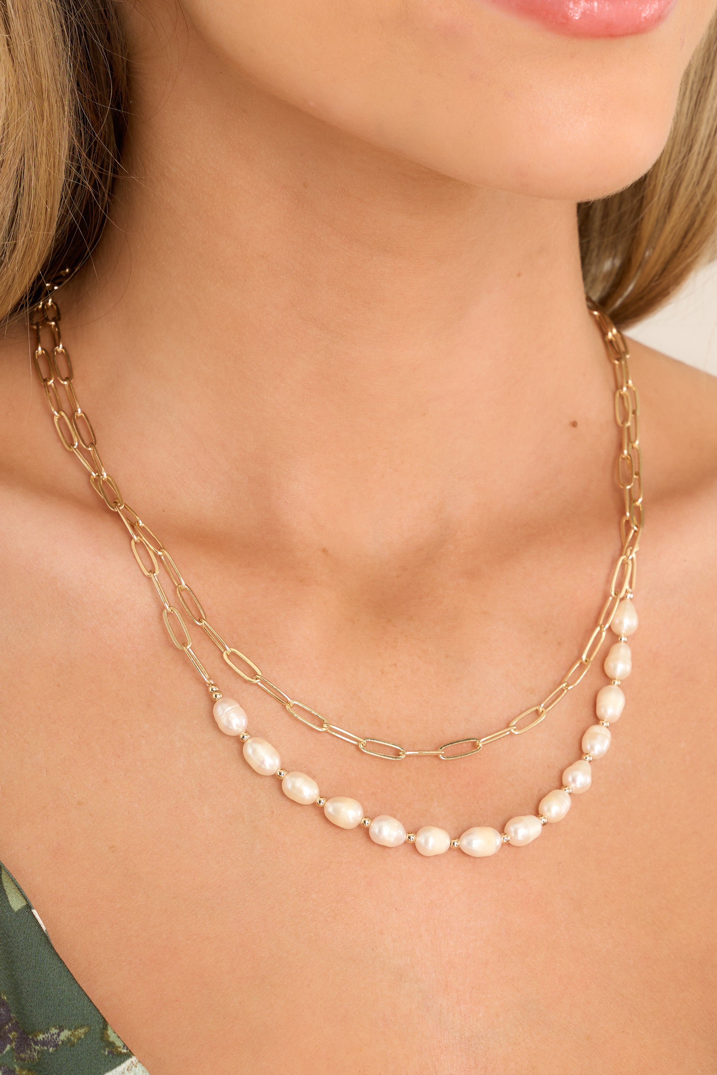 This gold and pearl necklace features gold hardware, 2 chains with thin links, and a row of faux pearls.