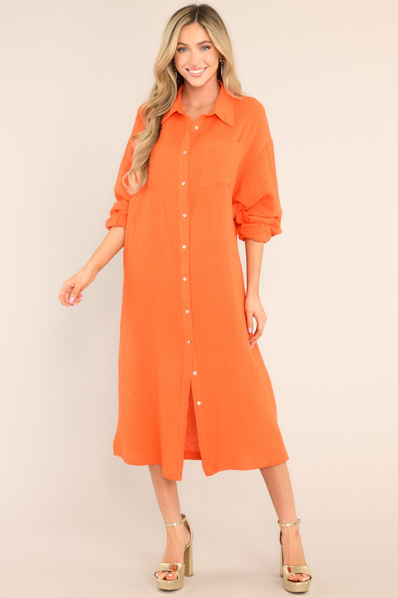 Full body view of this dress that features a collared neckline, functional buttons down the front, a front pocket on the left side of the bust, long sleeves with a cuff secured by a functional button, and two slits up the bottom hemline ending just below the knee.