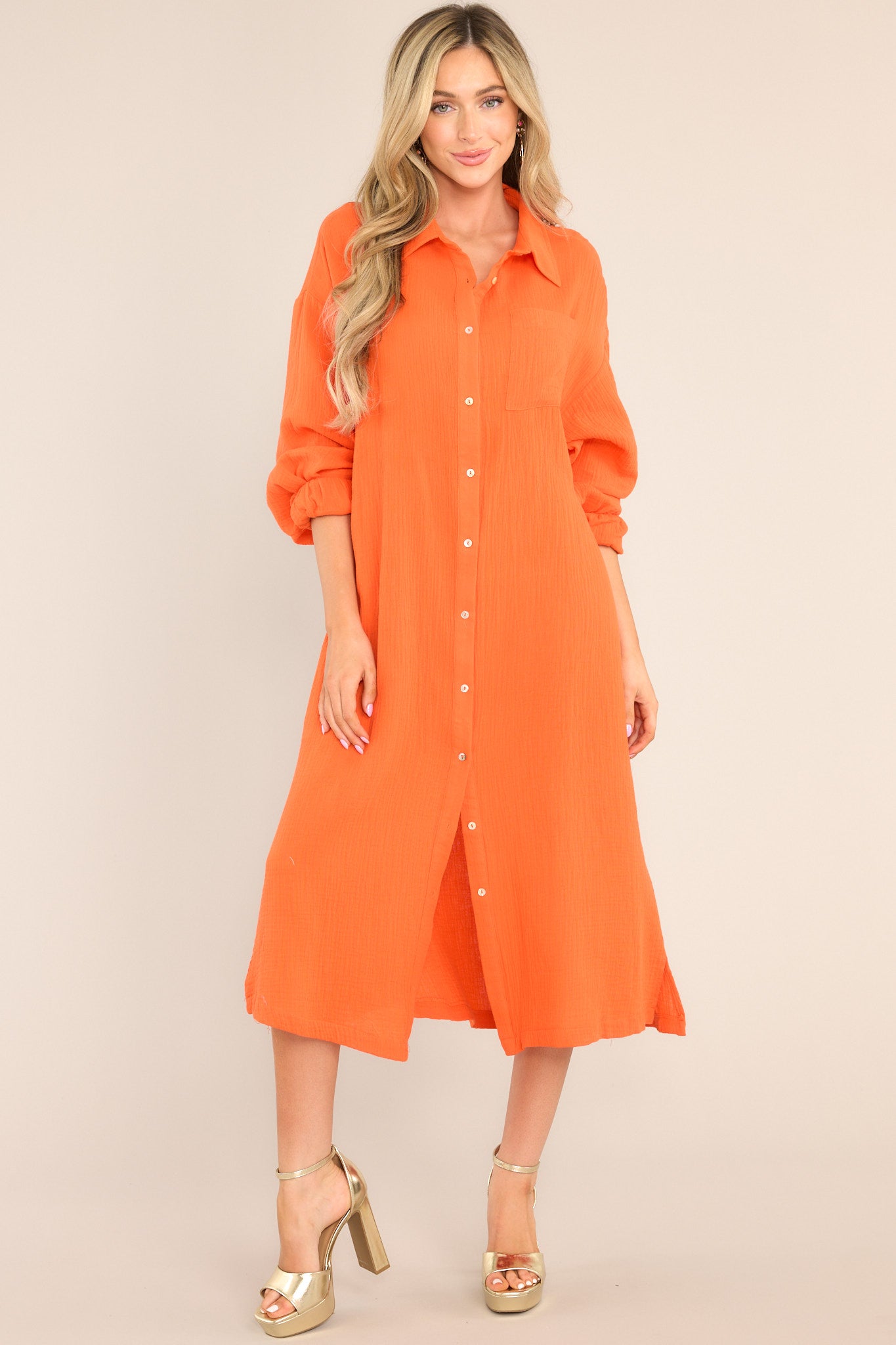 Front view of this dress that features a collared neckline, functional buttons down the front, a front pocket on the left side of the bust, long sleeves with a cuff secured by a functional button, and two slits up the bottom hemline ending just below the knee.