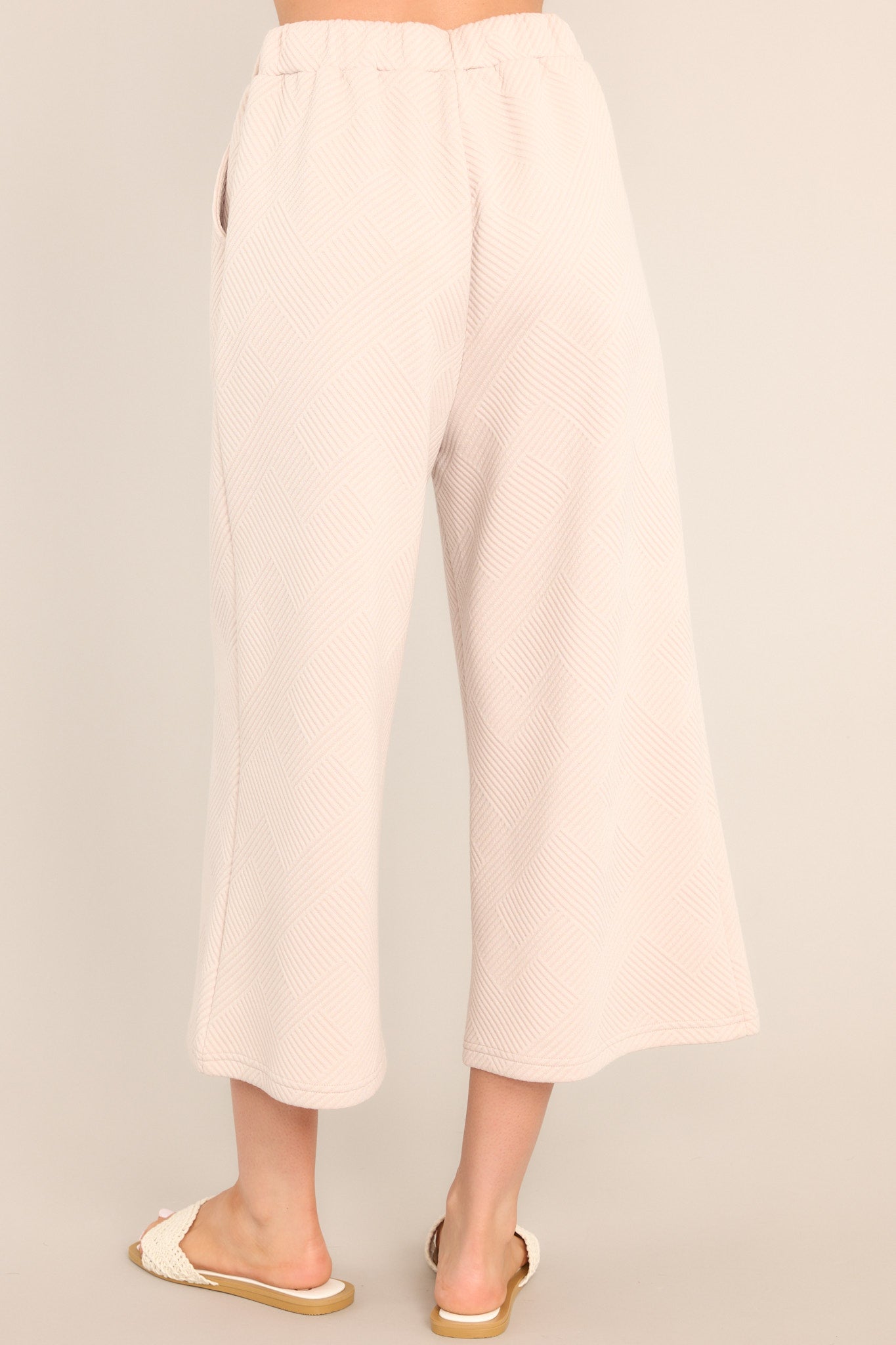 Back view of these pants that feature a high waisted design, an elastic waistband, functional hip pockets, a textured crisscross design, and a wide leg.