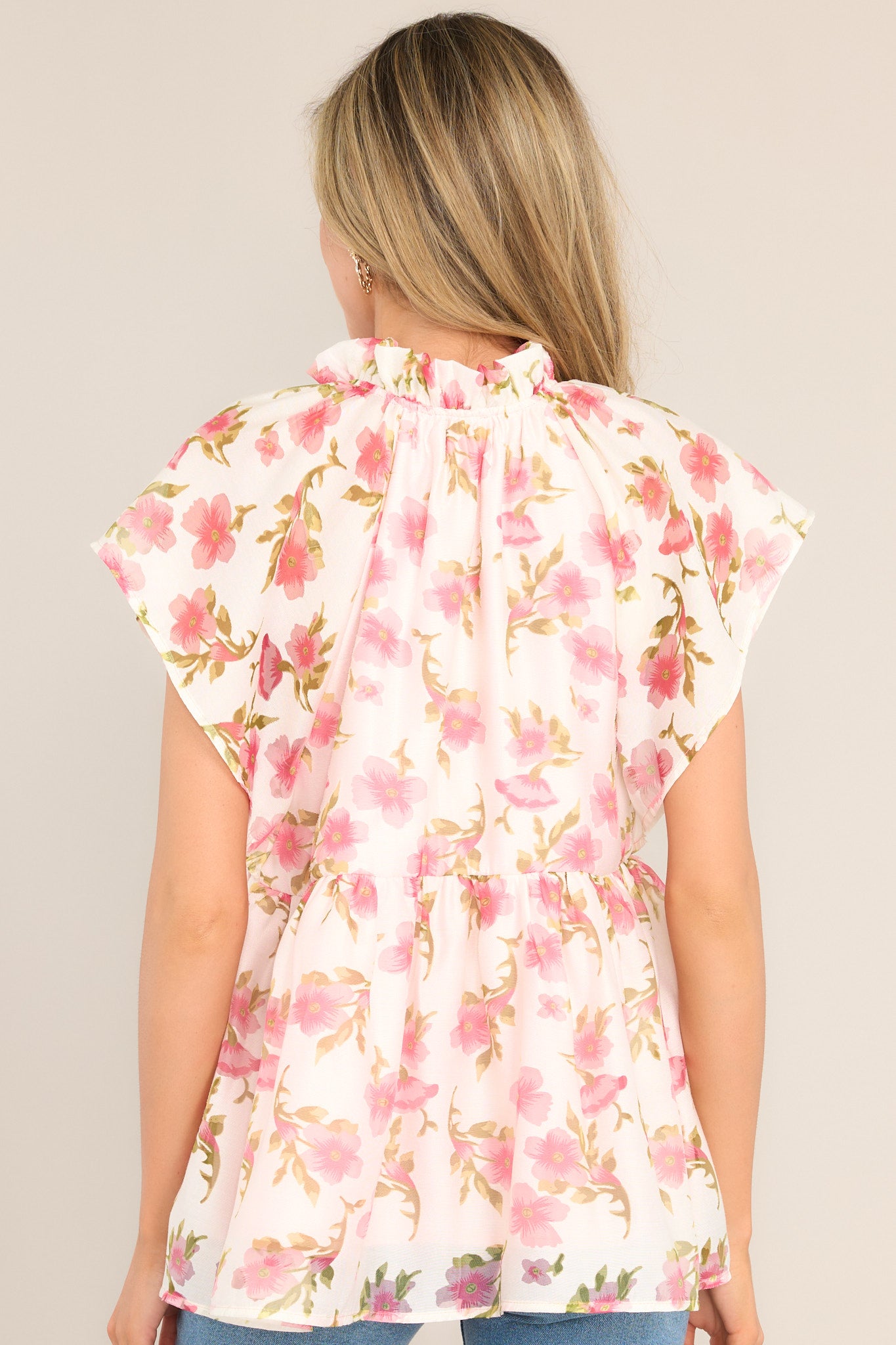 Back view of  this top that features a ruffled v-neckline, a flared waistline, wide transparent sleeves, and a delicate floral pattern.