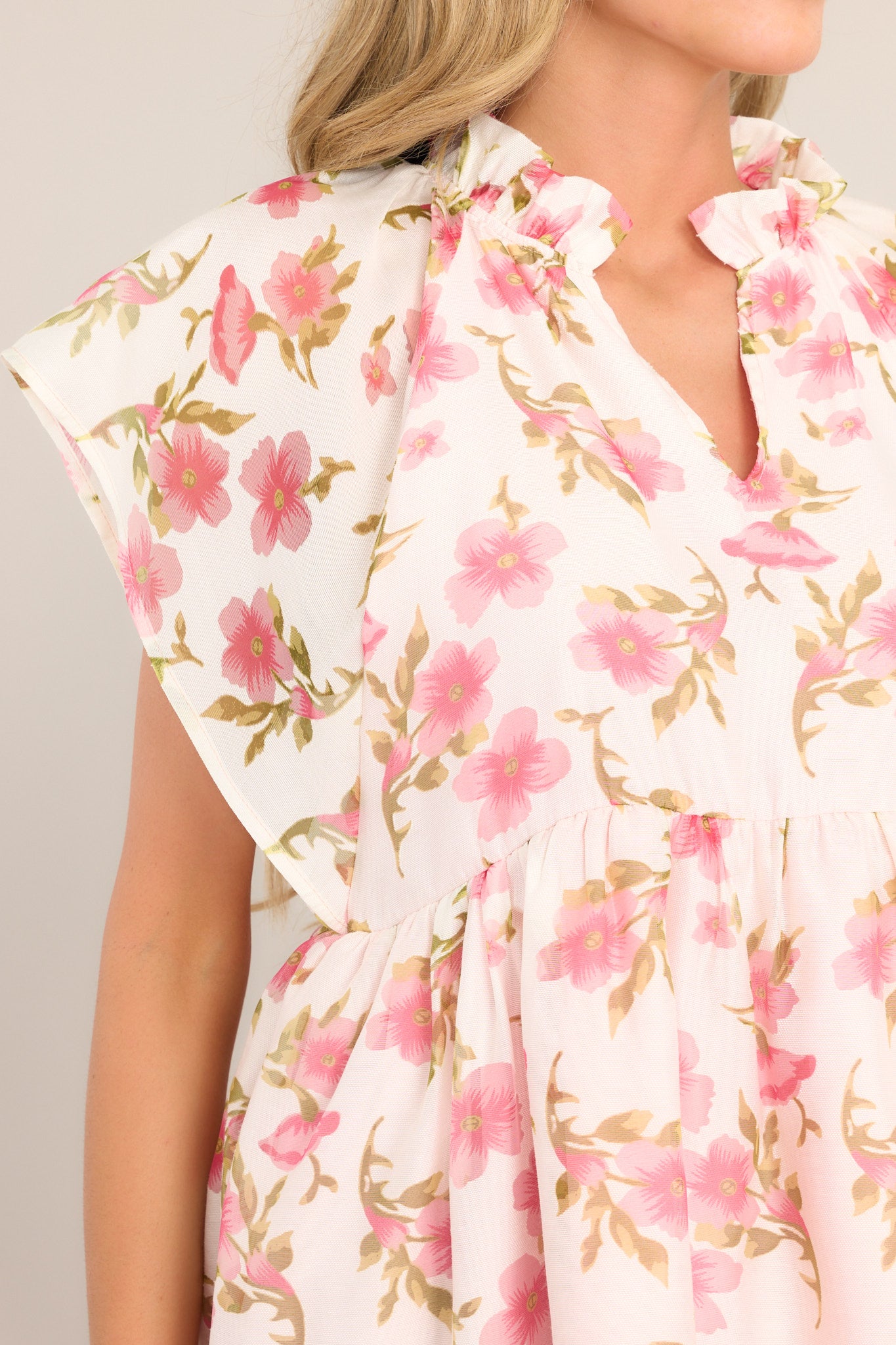 Close up view of this top that features a ruffled v-neckline, a flared waistline, wide transparent sleeves, and a delicate floral pattern.