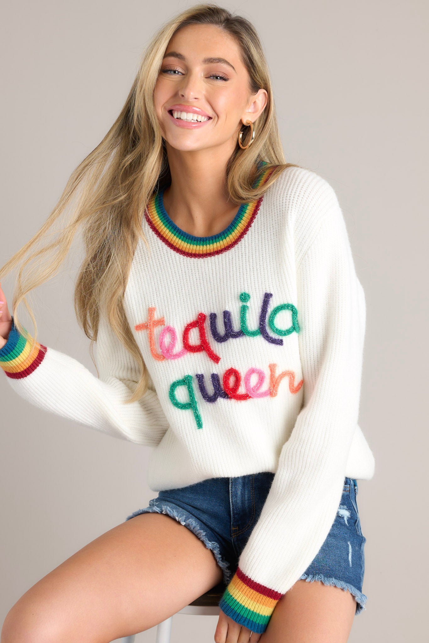 Front view of this sweater that features a crew neckline, textured wording, rainbow detailing, and cuffed sleeves.