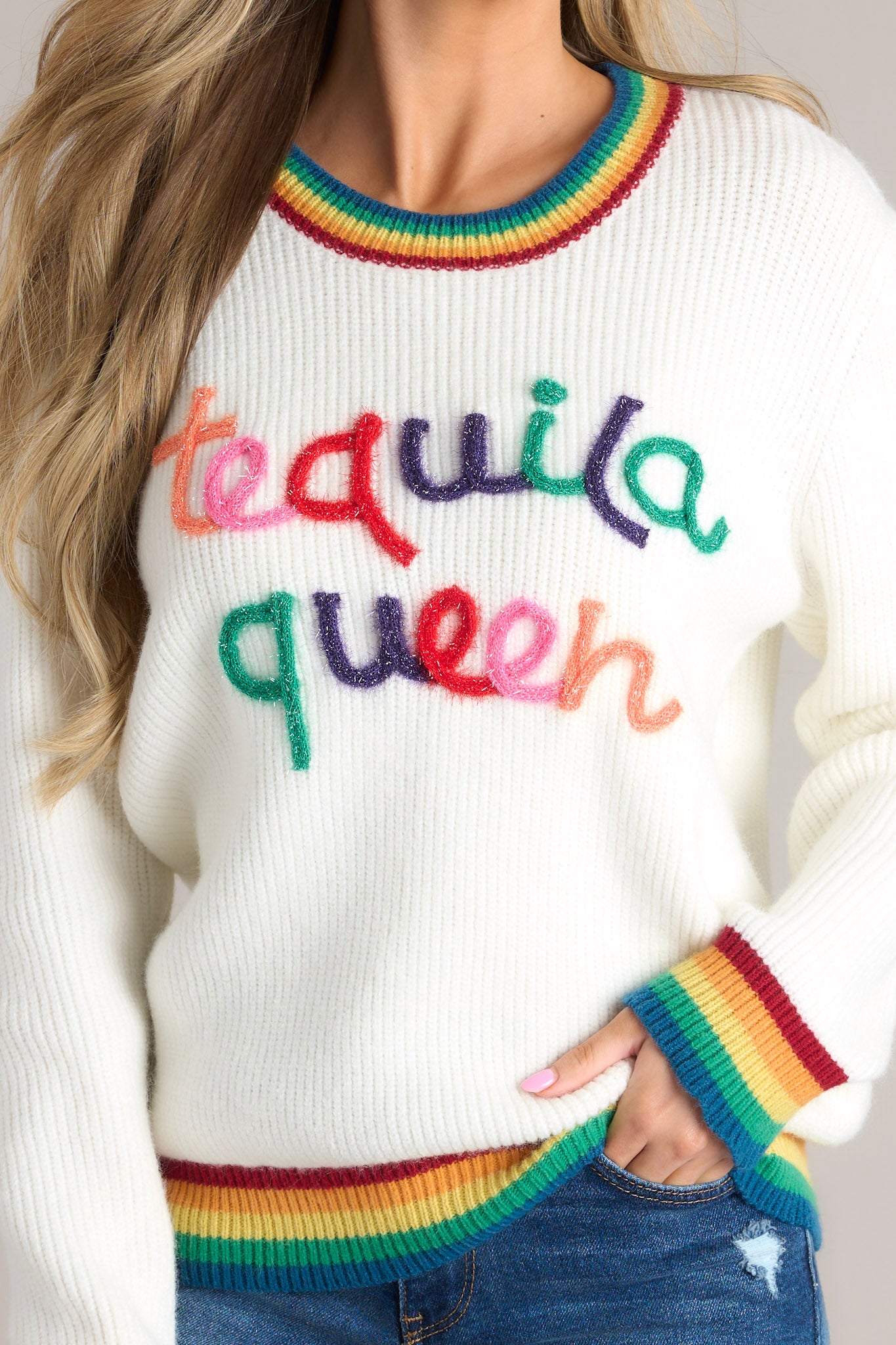 Close up view of this sweater that features a crew neckline, textured wording, rainbow detailing, and cuffed sleeves.