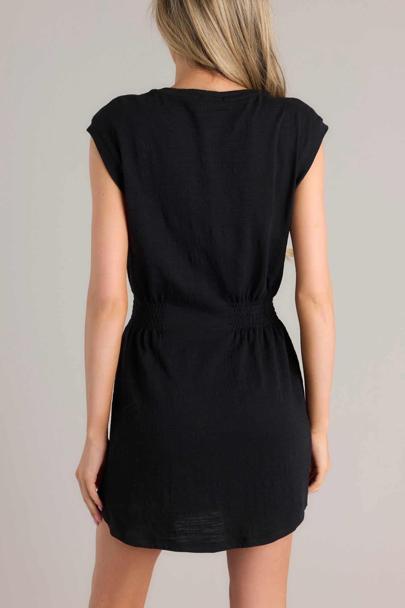 Back view of this dress that features a round neckline, smocked sections on either side of the waist, and a round hemline.