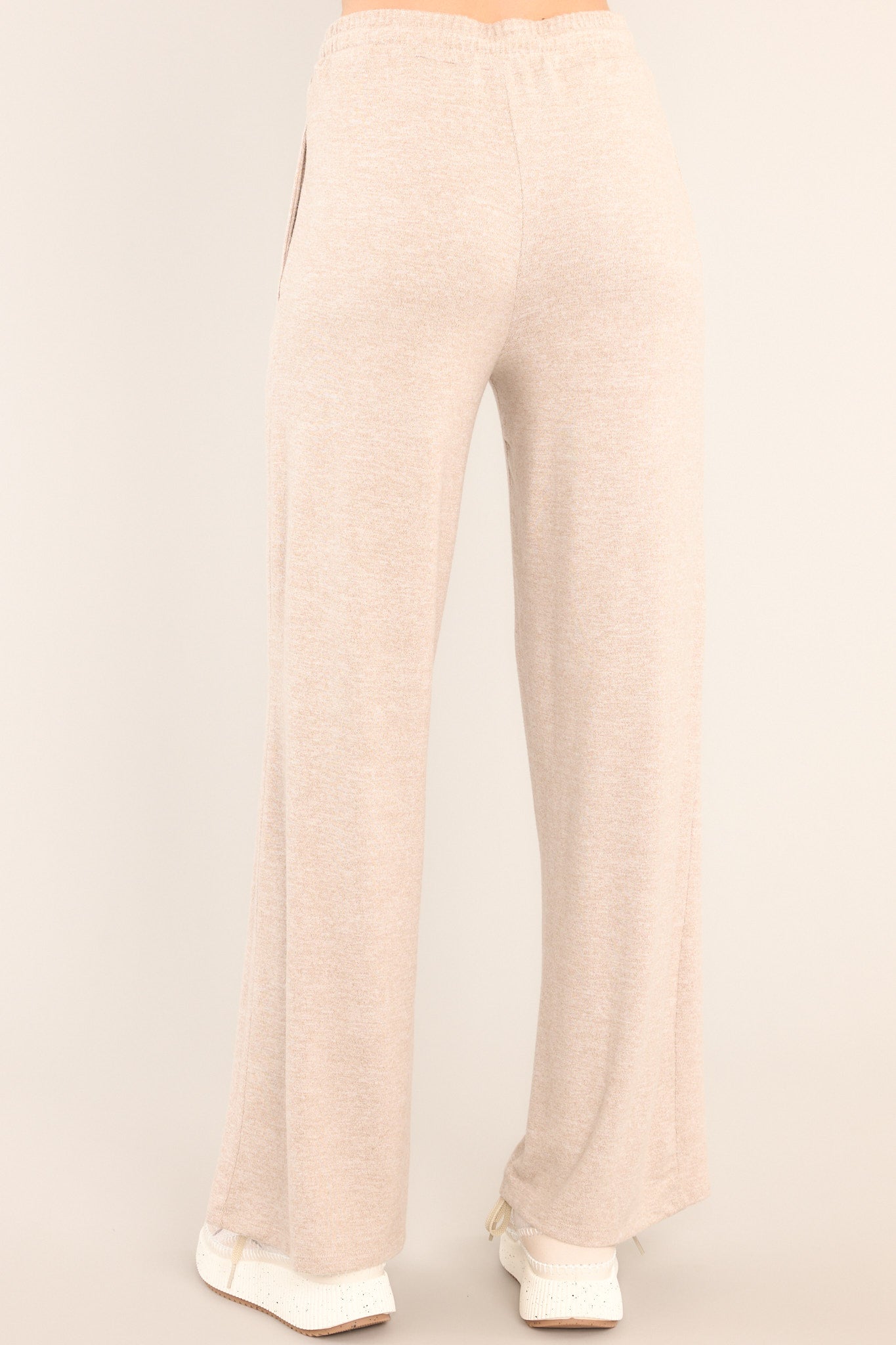 Back view of these tan lounge pants that feature an elastic waistband with a self-tie drawstring, pockets, and a wide leg.