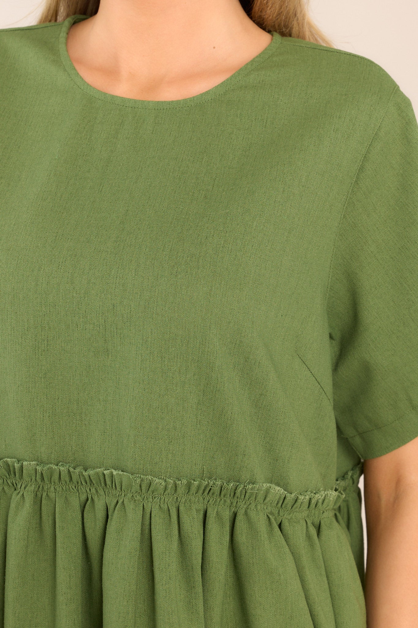 Close up view of this dress that features a round neckline, a keyhole cutout at the back of the neck with a button closure, short sleeves, ruffle detailing along the waistline, and functional pockets at the hips. 