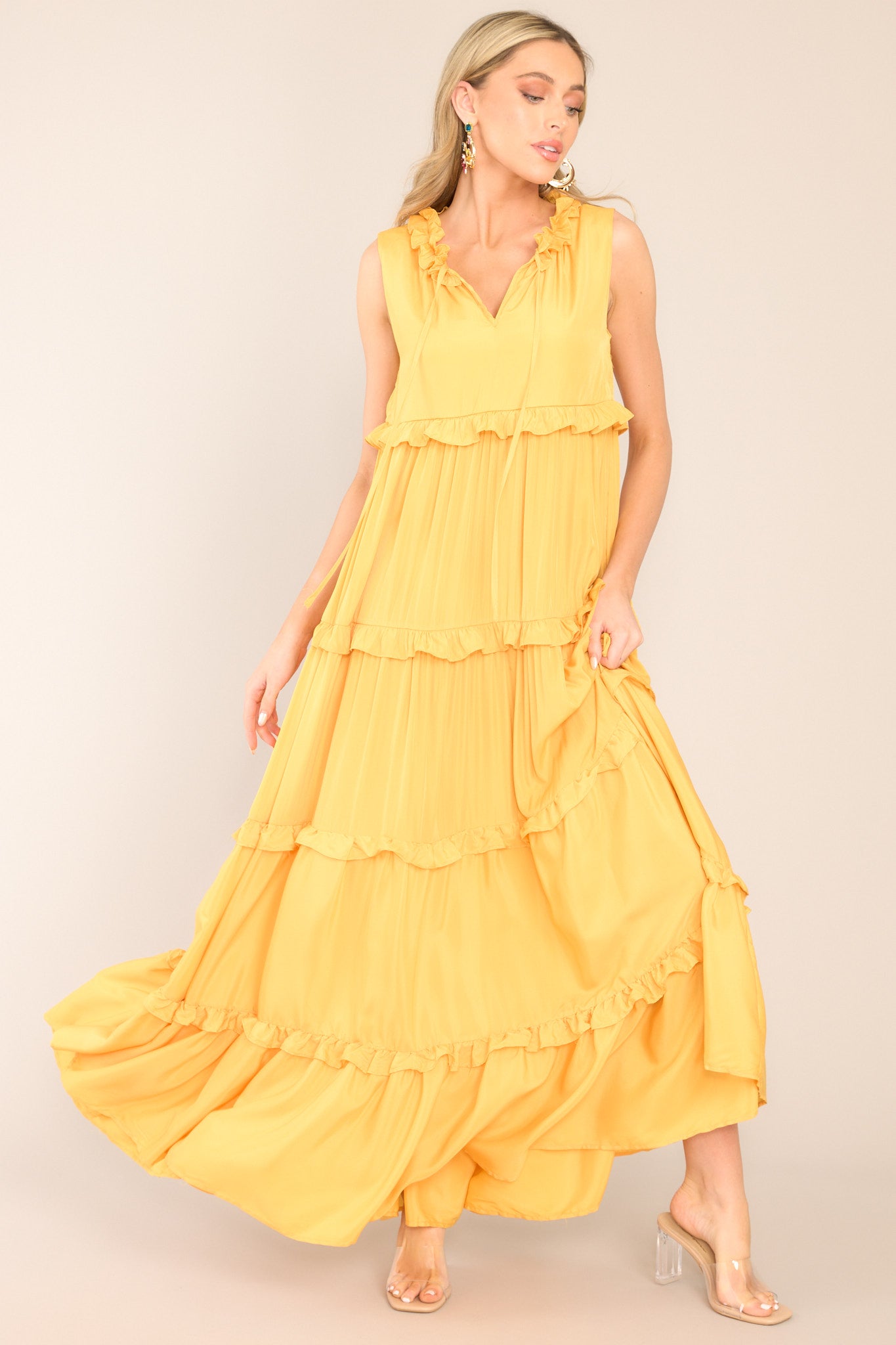 This dress features a ruffled v-neckline with a self-tie closure, a sleeveless design, and a flowy skirt with subtle ruffle detailing throughout.