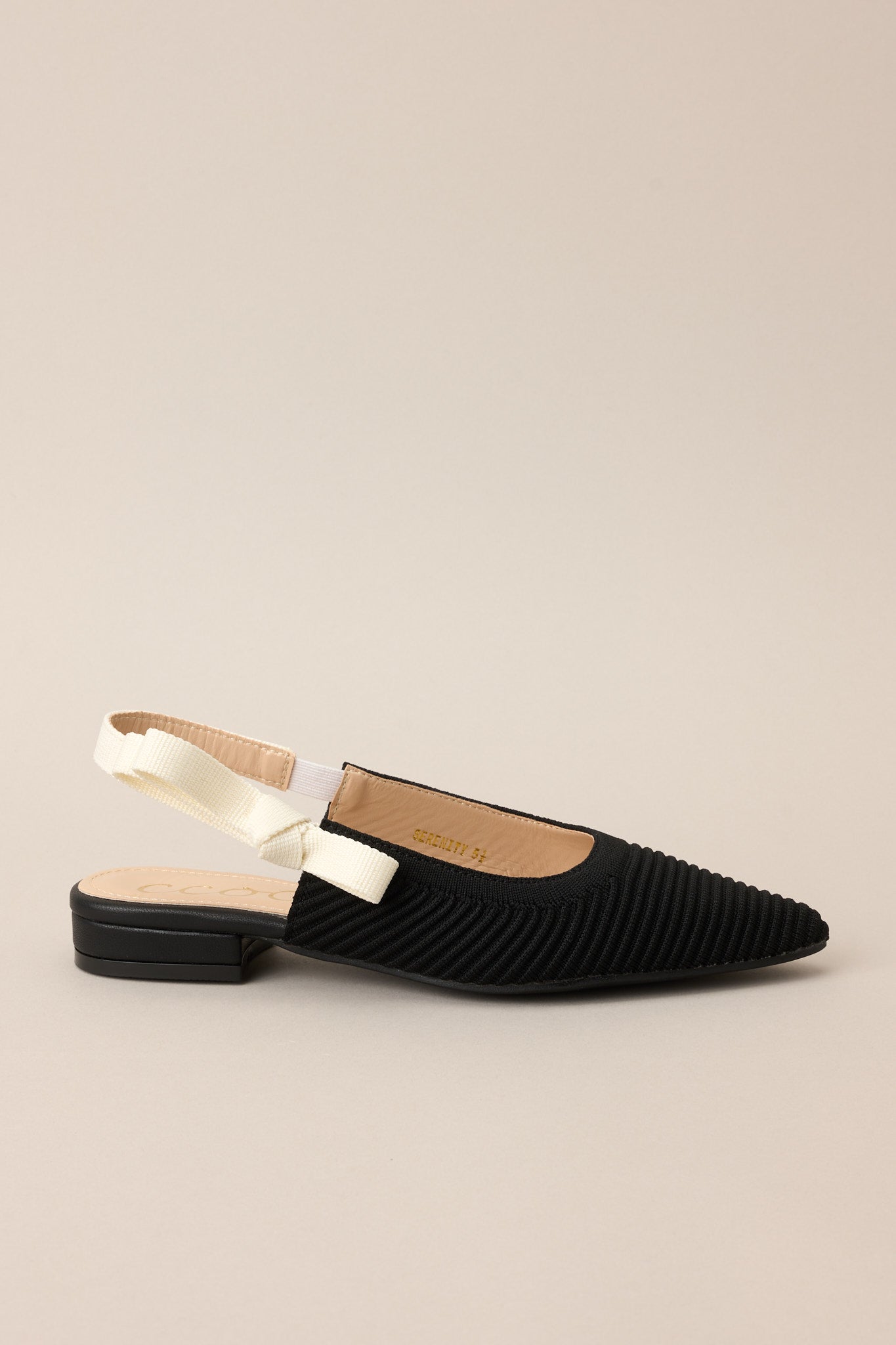 Side view of these shoes that feature a pointed toe, a textured material, a contrasting elastic strap around the back of the heel, and a subtle bow detail.