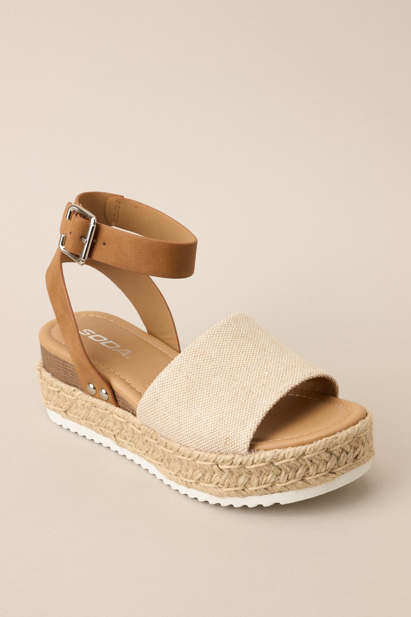 Angled front view of these sandals that feature a rounded toe, silver hardware, a textured strap over the top of the foot, a contrasting strap around the heel and ankle, and a buckle closure.