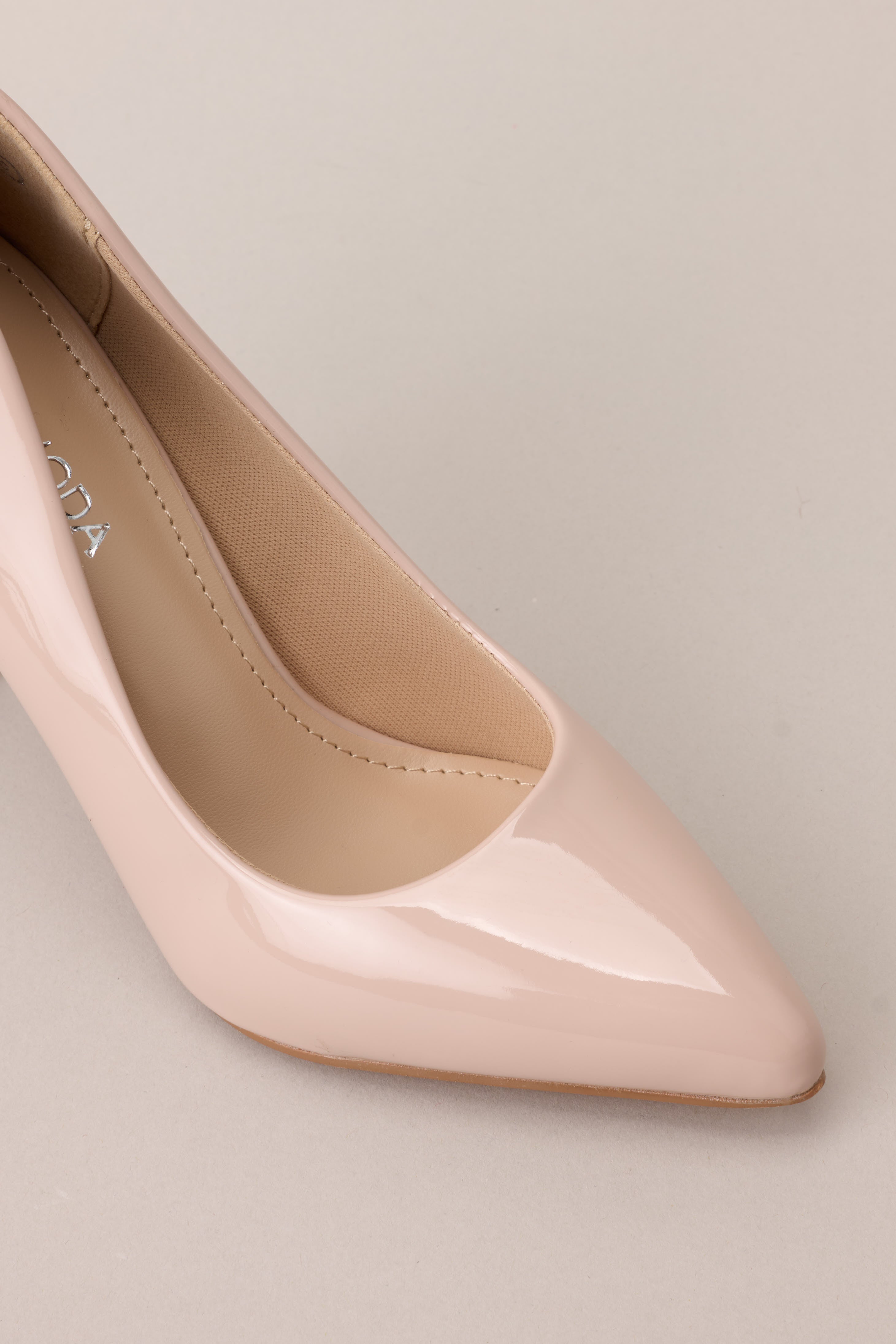 Close up view of the toe of these Beige heels with a pointed toe, vibrant color, glossy finish, and skinny heel.
