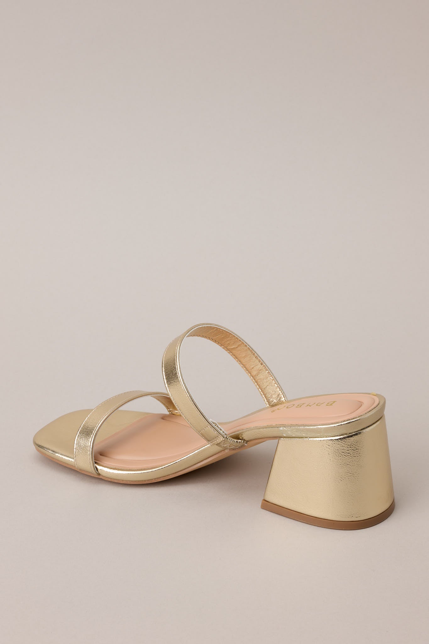 Back view of these gold block heels that feature a square toe, two gold straps across the top of the foot, and a block heel.