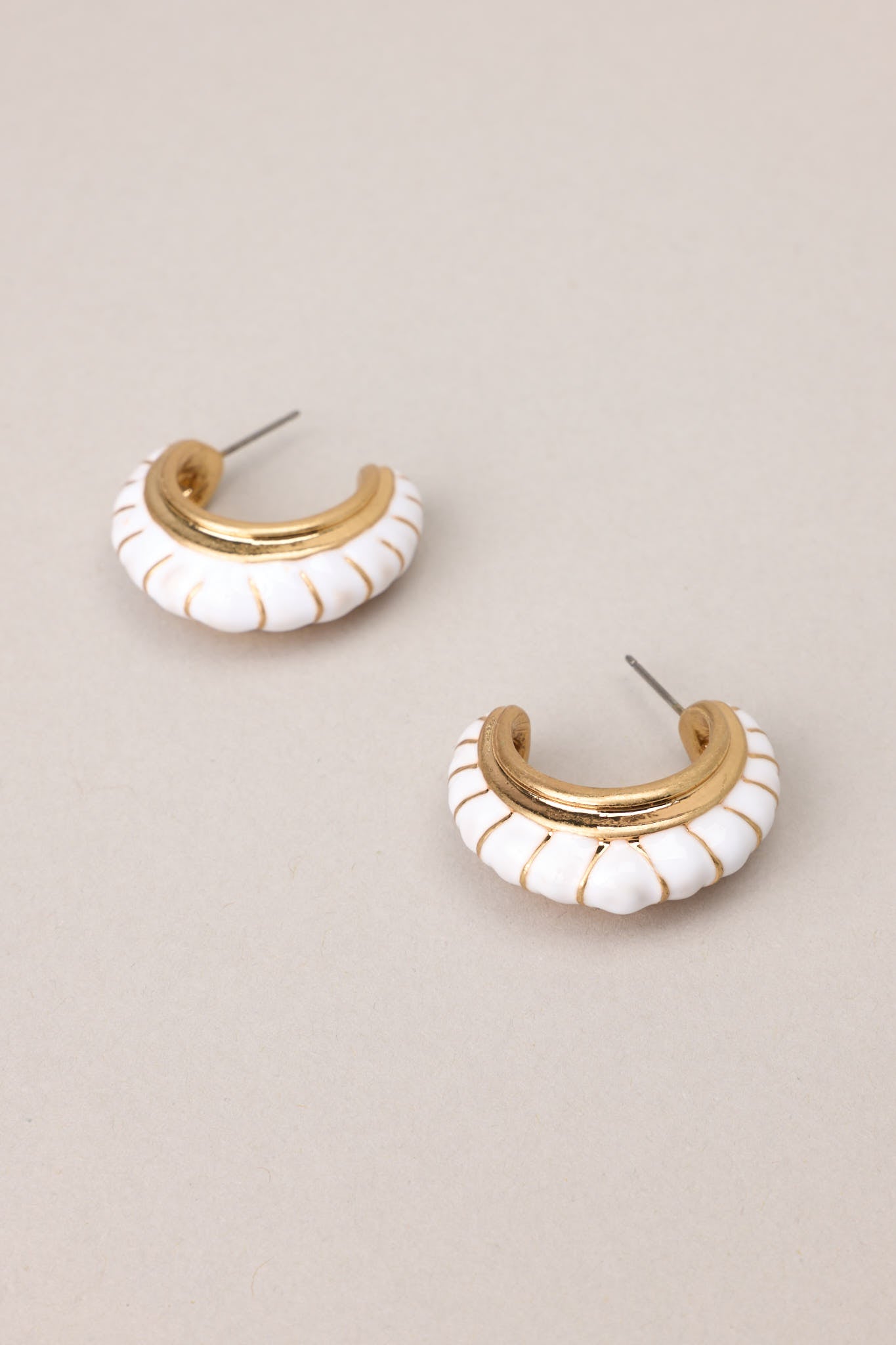 Angled overview of these gold earrings with white detailing, secure post backings.
