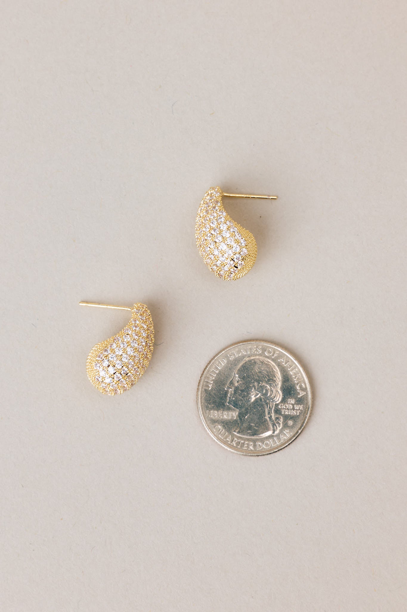 Size comparison of a quarter to these tear shaped yellow gold earring with mini rhinestones covering it, and gold hardware.