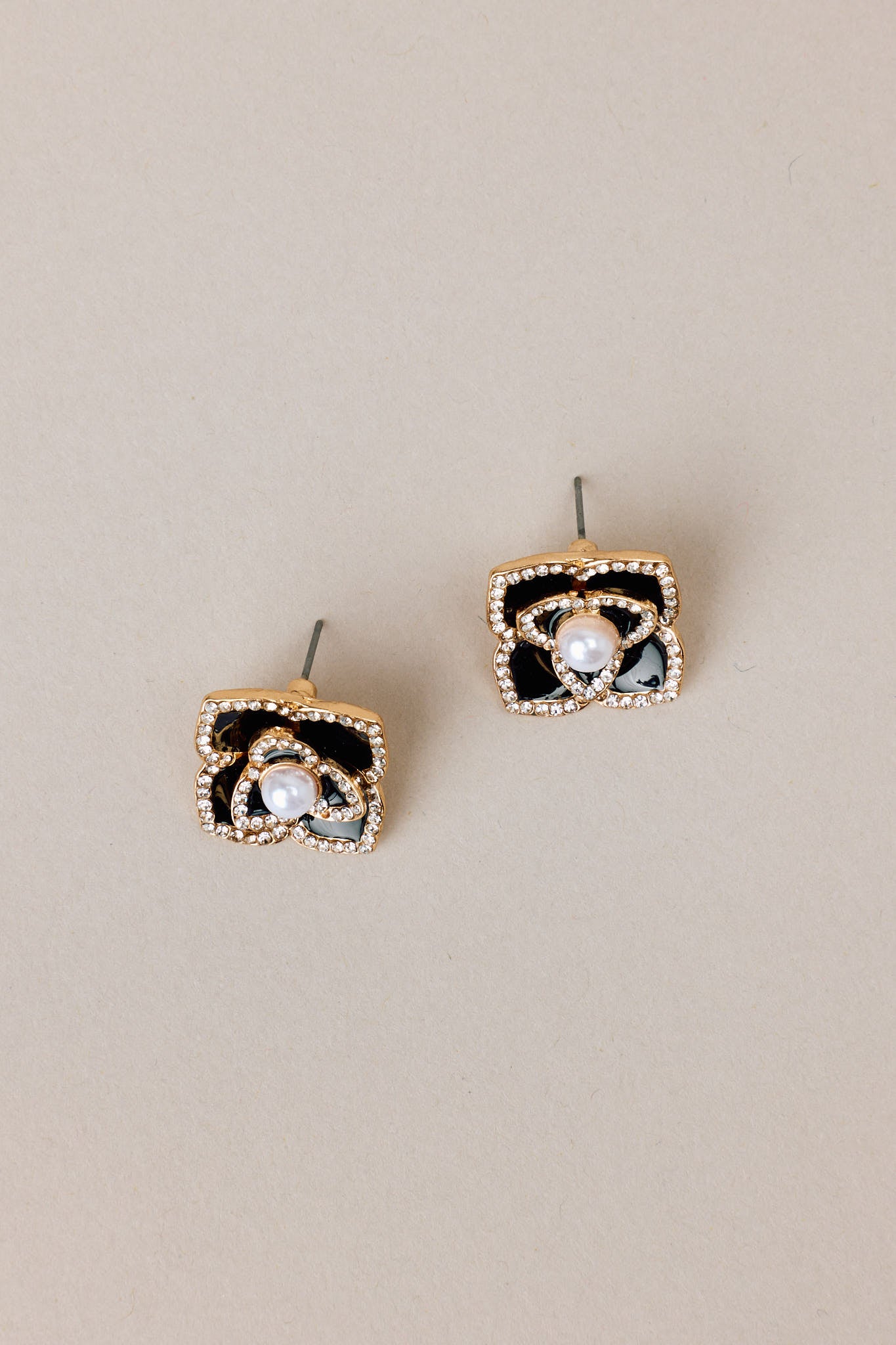 Overhead side view of these black pearl earrings that feature gold hardware, a flower design, rhinestone embellishments, a faux pearl detail, and a secure post backing.