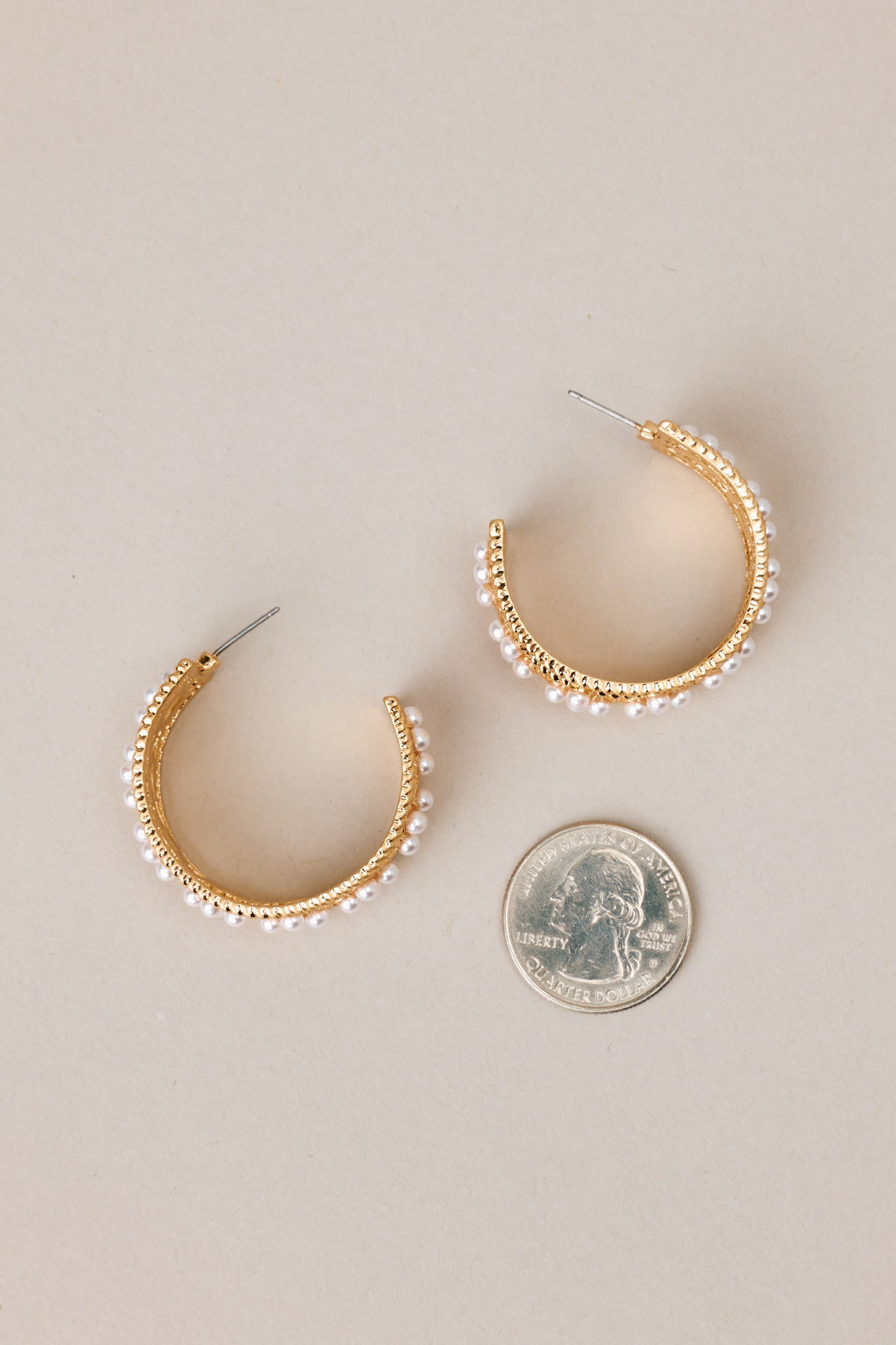 Size comparison of these hoops that feature gold hardware, faux pearl embellishments, and secure post backings.