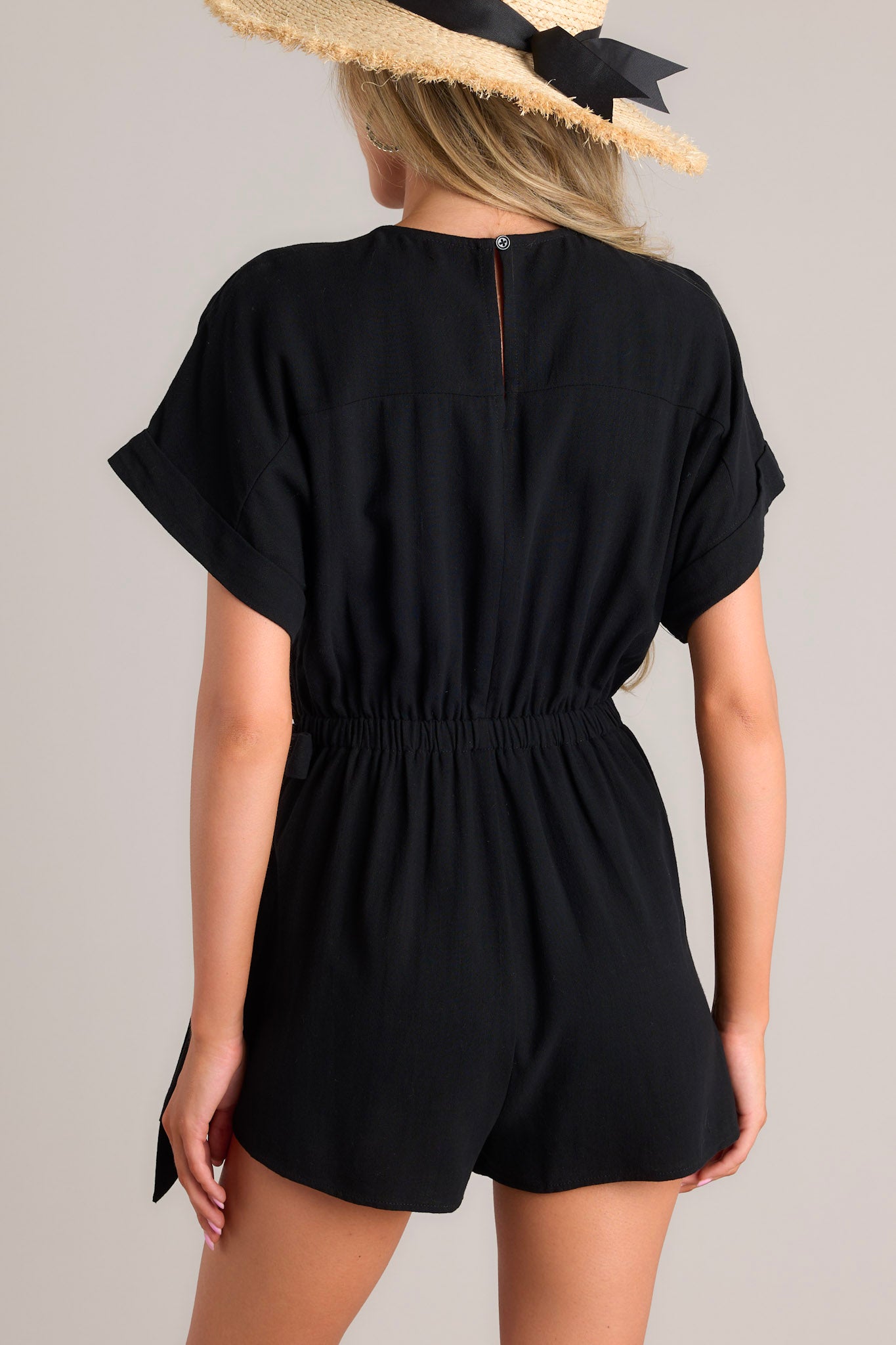 Back view of this romper that features a V-shaped neckline, a keyhole back with button closure, cuffed sleeves, and a faux wrap.