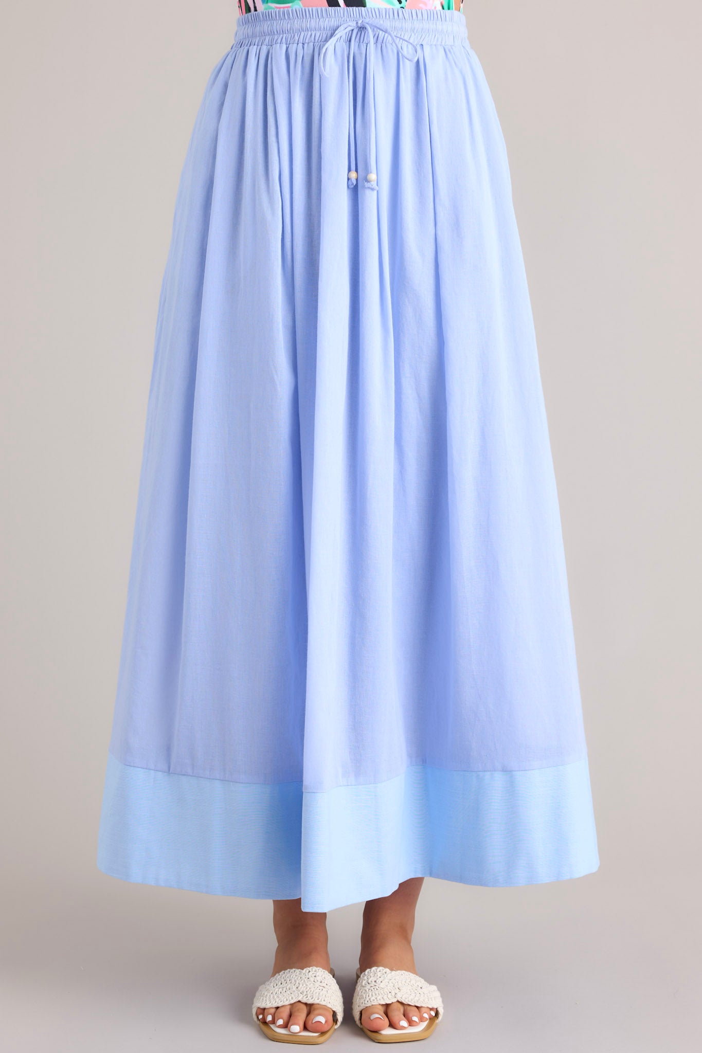 Close up front view of this skirt that features a high waisted design, an elastic waistband, a self-tie drawstring, functional pockets, flowing fabric, and a thick hemline.