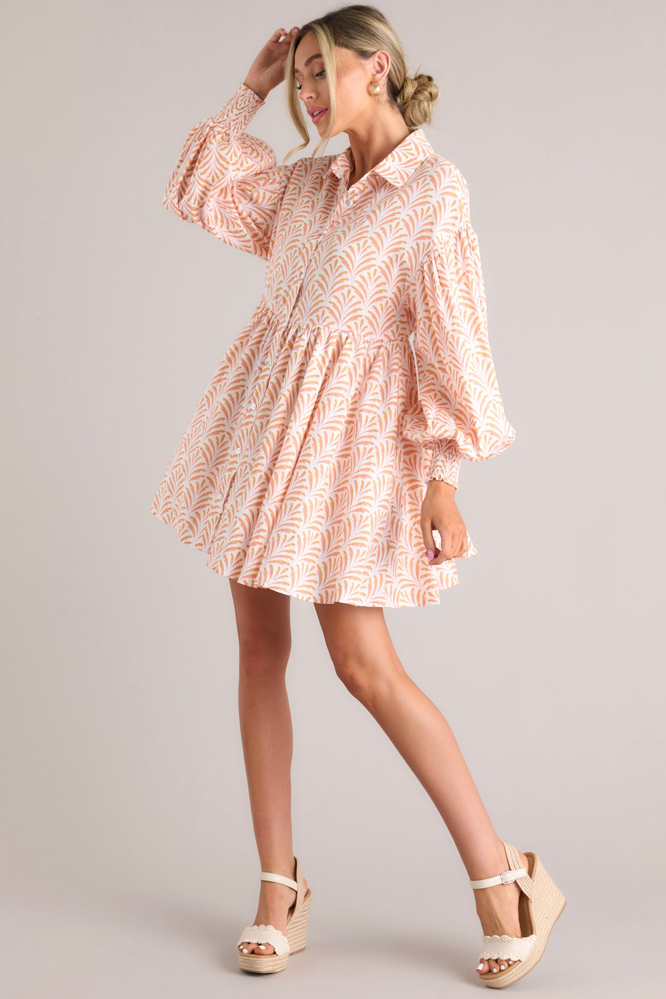 This orange and white dress features a collared neckline, functional buttons down the front, long sleeves with smocked cuffs, and a flowy, relaxed fit throughout.