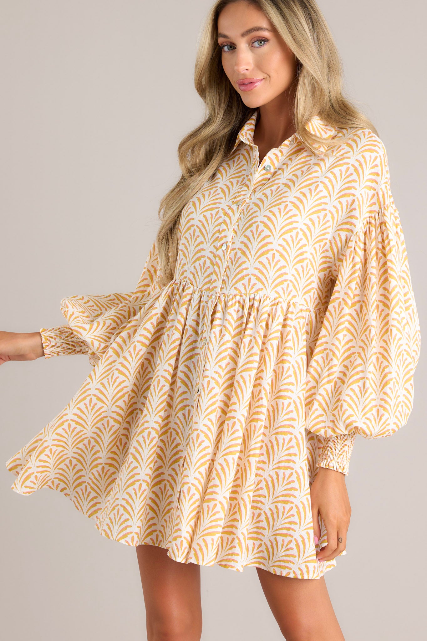 Front view of this dress that features a collared neckline, functional buttons down the front, long sleeves with smocked cuffs, and a flowy, relaxed fit throughout.