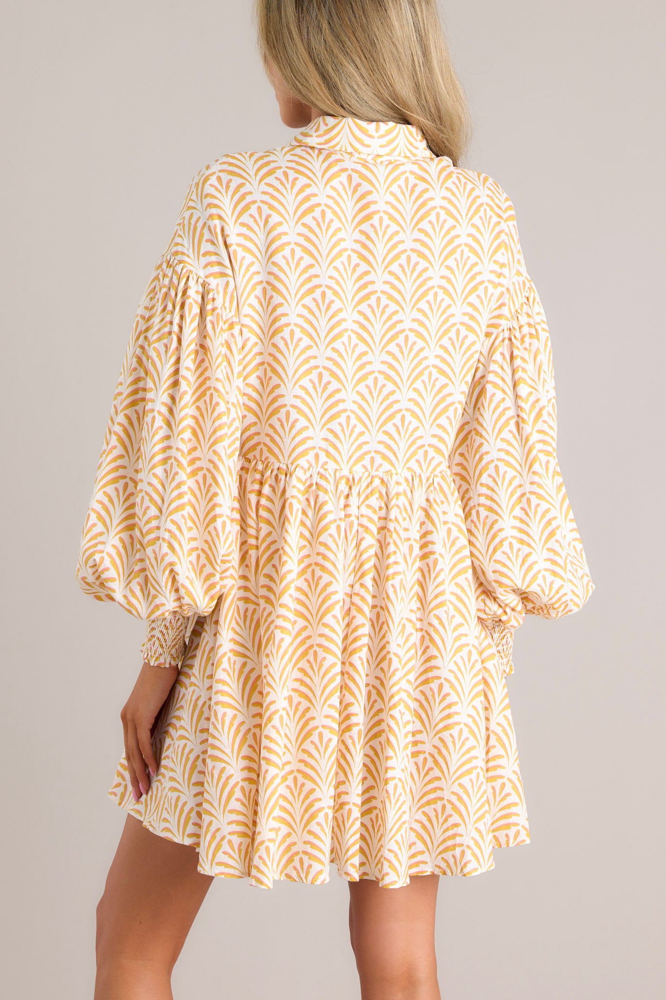 Back view of this dress that features a collared neckline, functional buttons down the front, long sleeves with smocked cuffs, and a flowy, relaxed fit throughout.