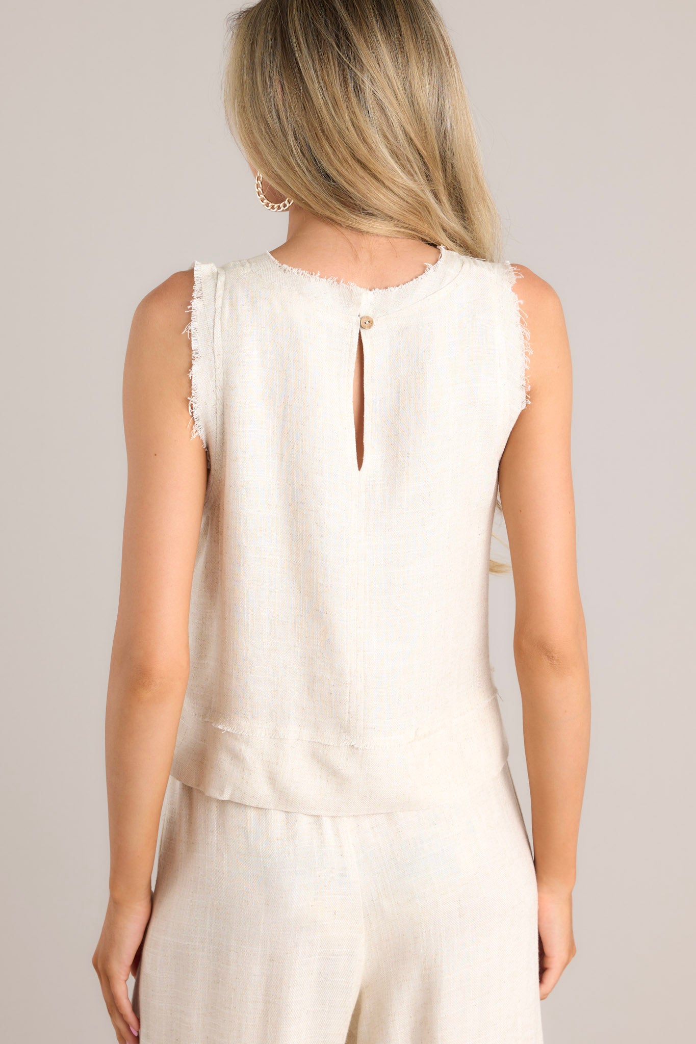 Back view of this tank that features a raw crew neckline, a keyhole with a button closure, a lightweight fabric, a split hemline, and a slightly cropped length.