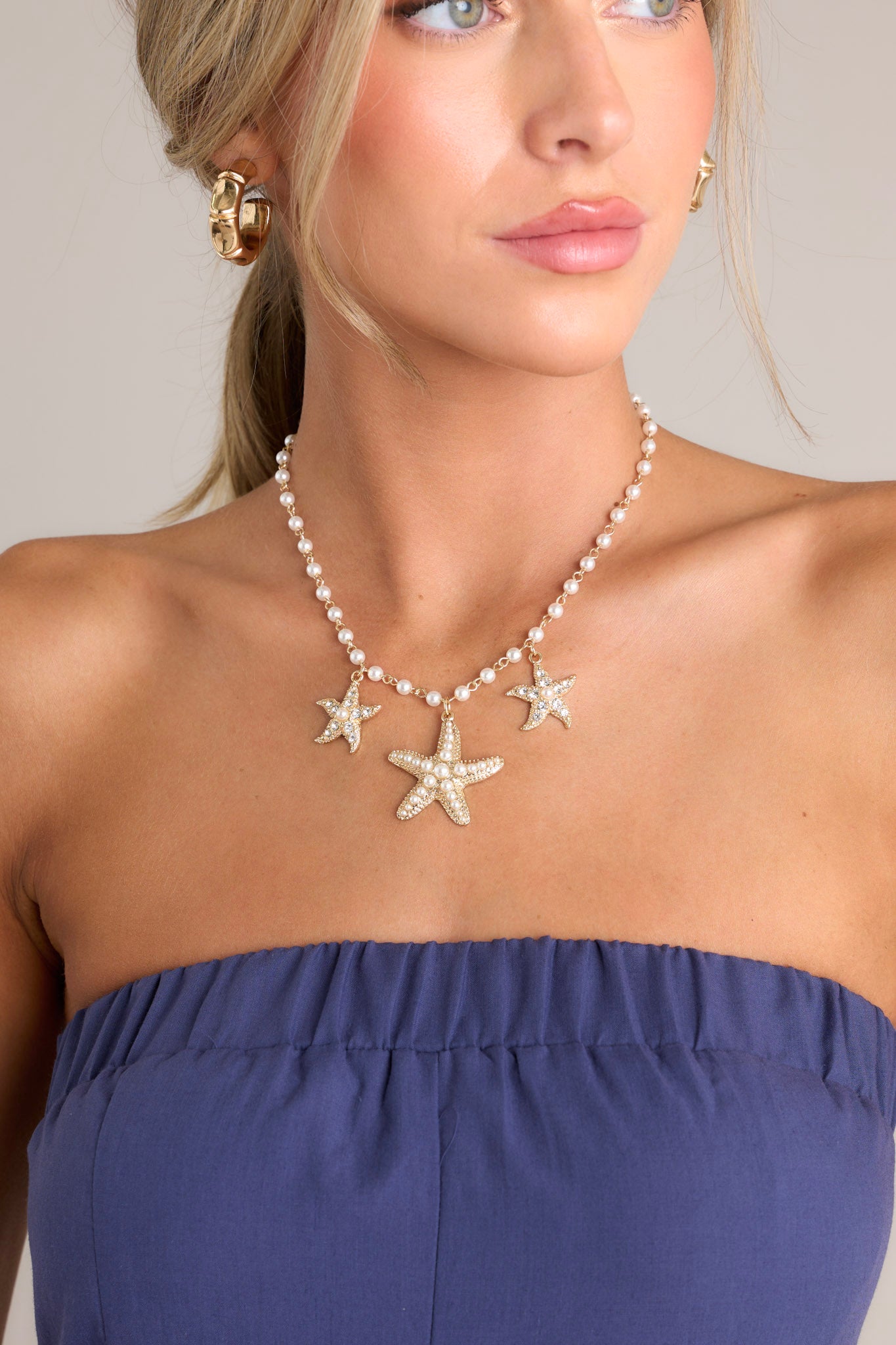 This necklace features gold hardware, faux pearls, and rhinestone & faux pearl embellished starfish pendants.