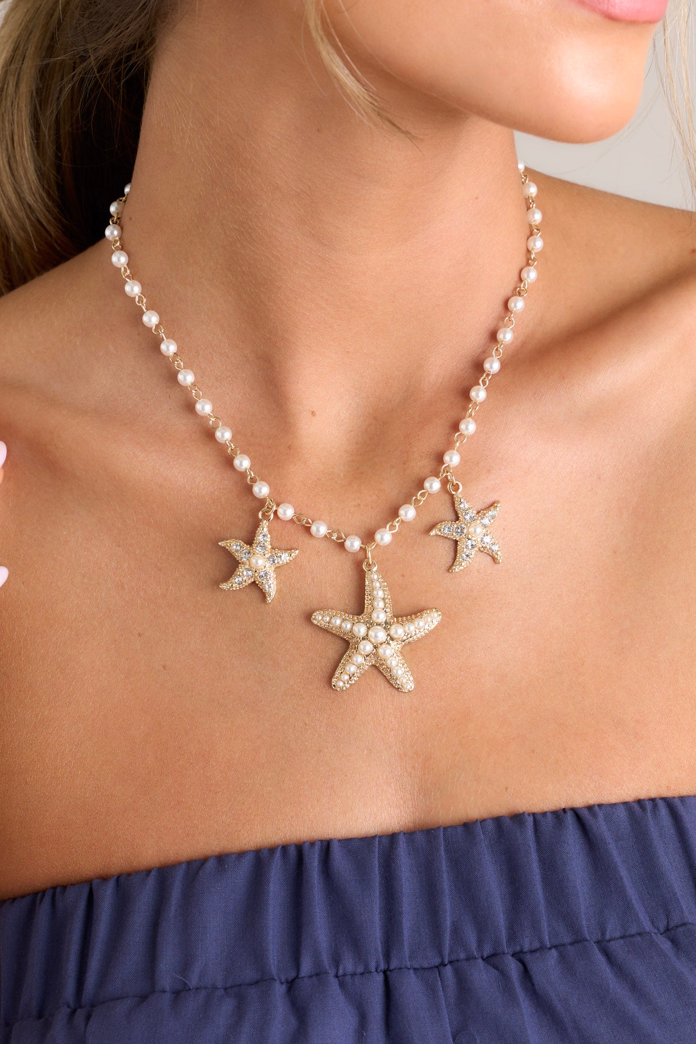 Close up view of this necklace that features gold hardware, faux pearls, and rhinestone & faux pearl embellished starfish pendants.