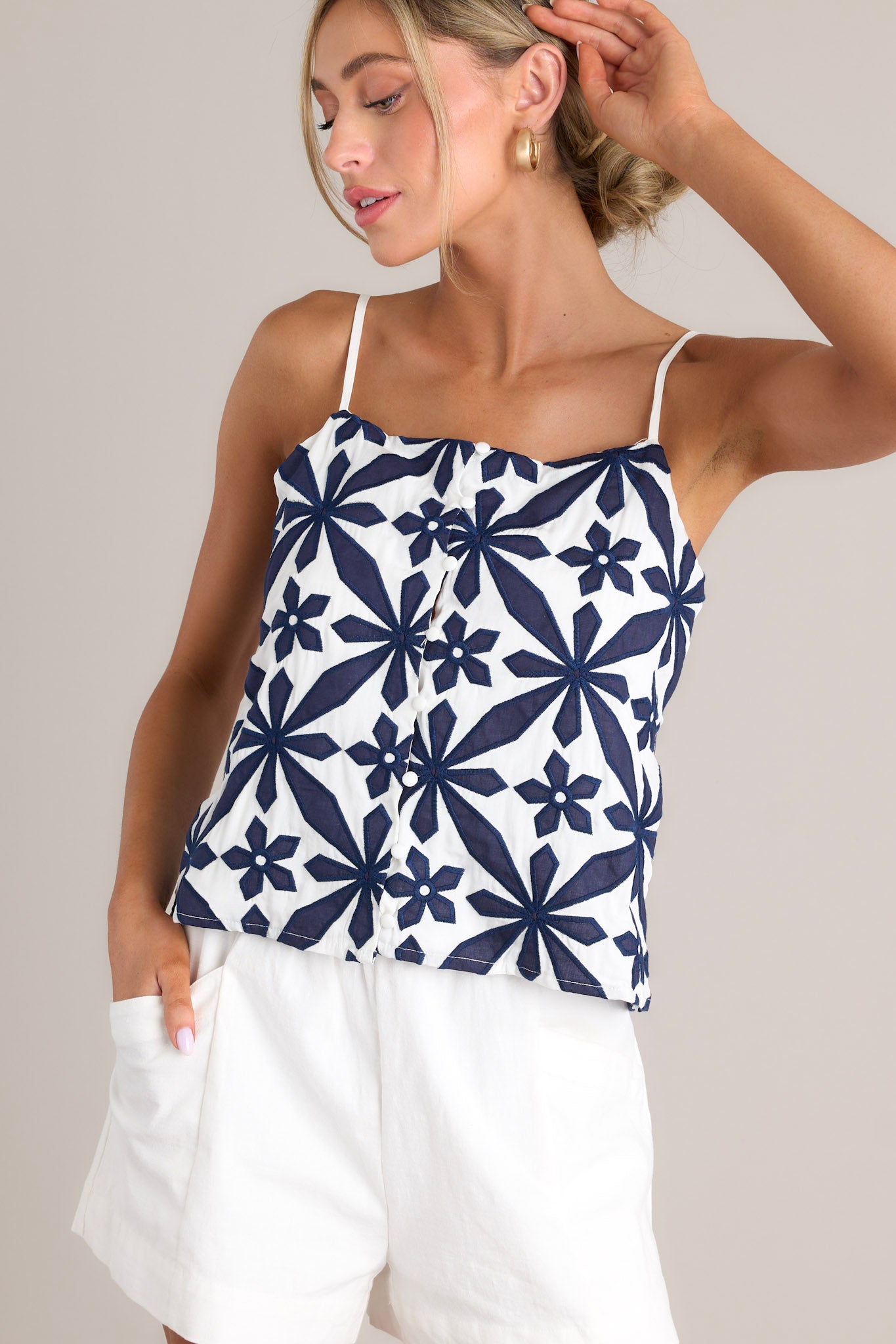 Full view of this top that features a square neckline, thin adjustable straps, a functional button front, an embroidered geometric floral pattern, and a cropped hemline.