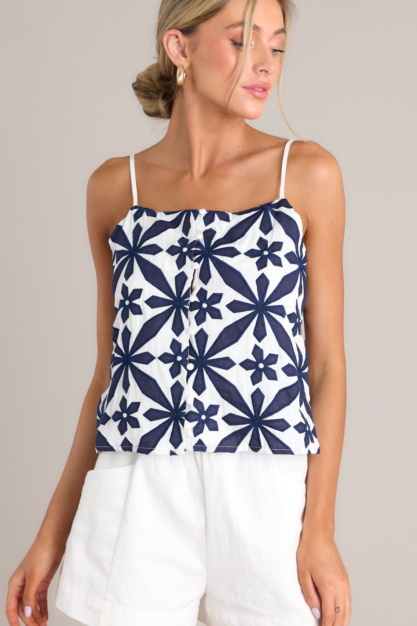 Front view of this top that features a square neckline, thin adjustable straps, a functional button front, an embroidered geometric floral pattern, and a cropped hemline.