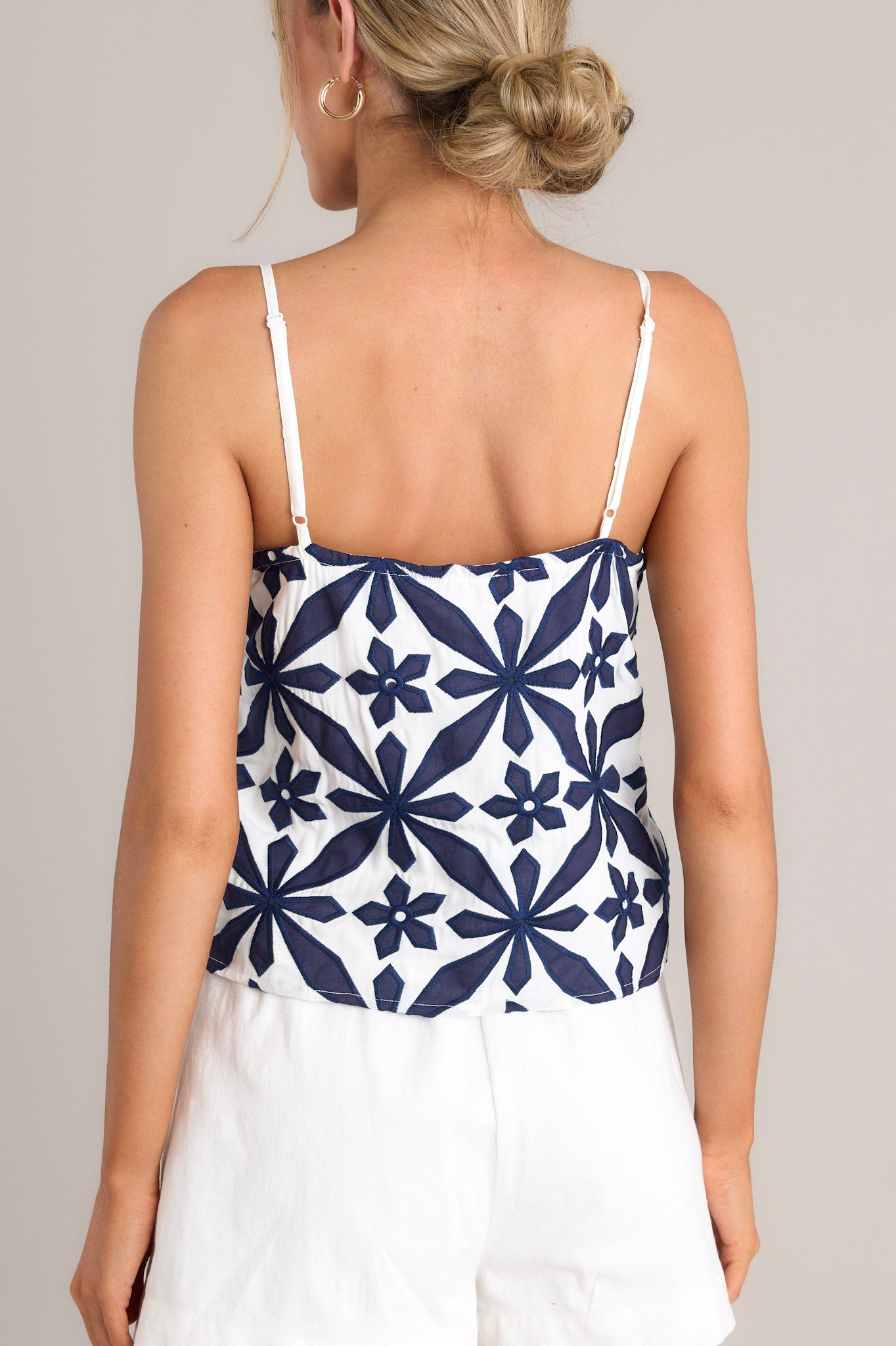 Back view of this top that features a square neckline, thin adjustable straps, a functional button front, an embroidered geometric floral pattern, and a cropped hemline.