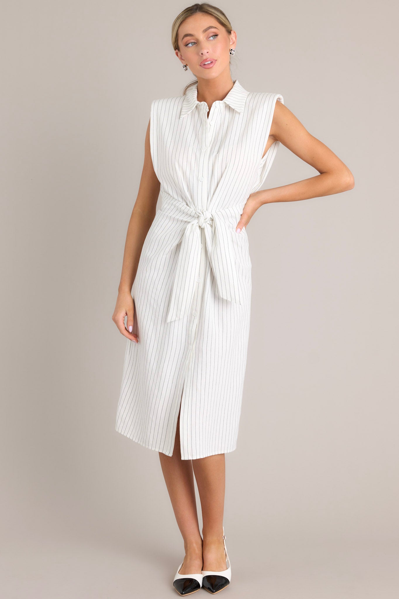 This pinstripe midi dress features a collared neckline, shoulder padding, a functional button front, a self-tie waist feature, an elastic insert at the back of the waist, and a front slit.