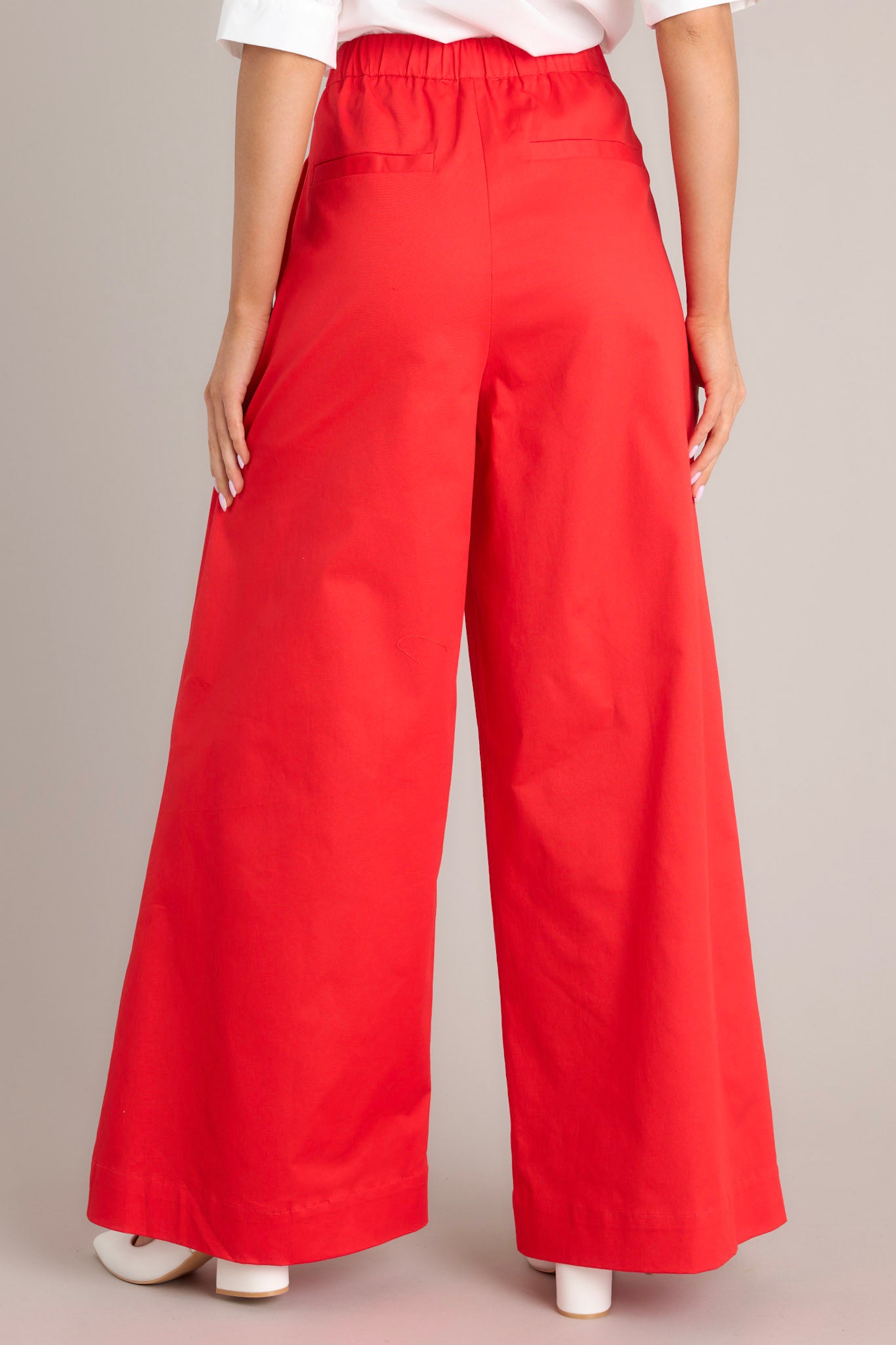 Back view of these pants that feature a high waisted design, an elastic insert, a discrete side zipper, subtle pleats, functional hip pockets, faux back pockets, and a thick hemline.