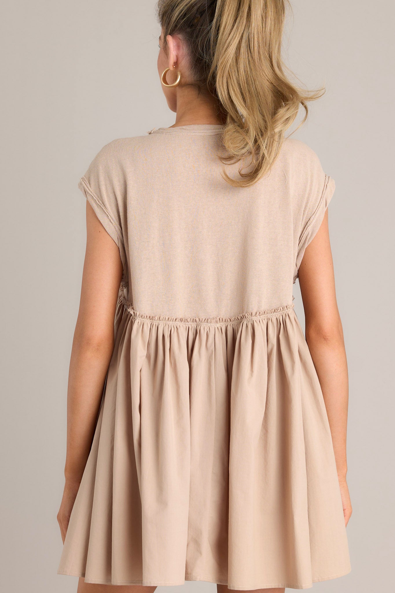 Back  view of this tan mini dress that features a crew neckline, contrasting materials, functional pockets, and folded cuffed sleeves.