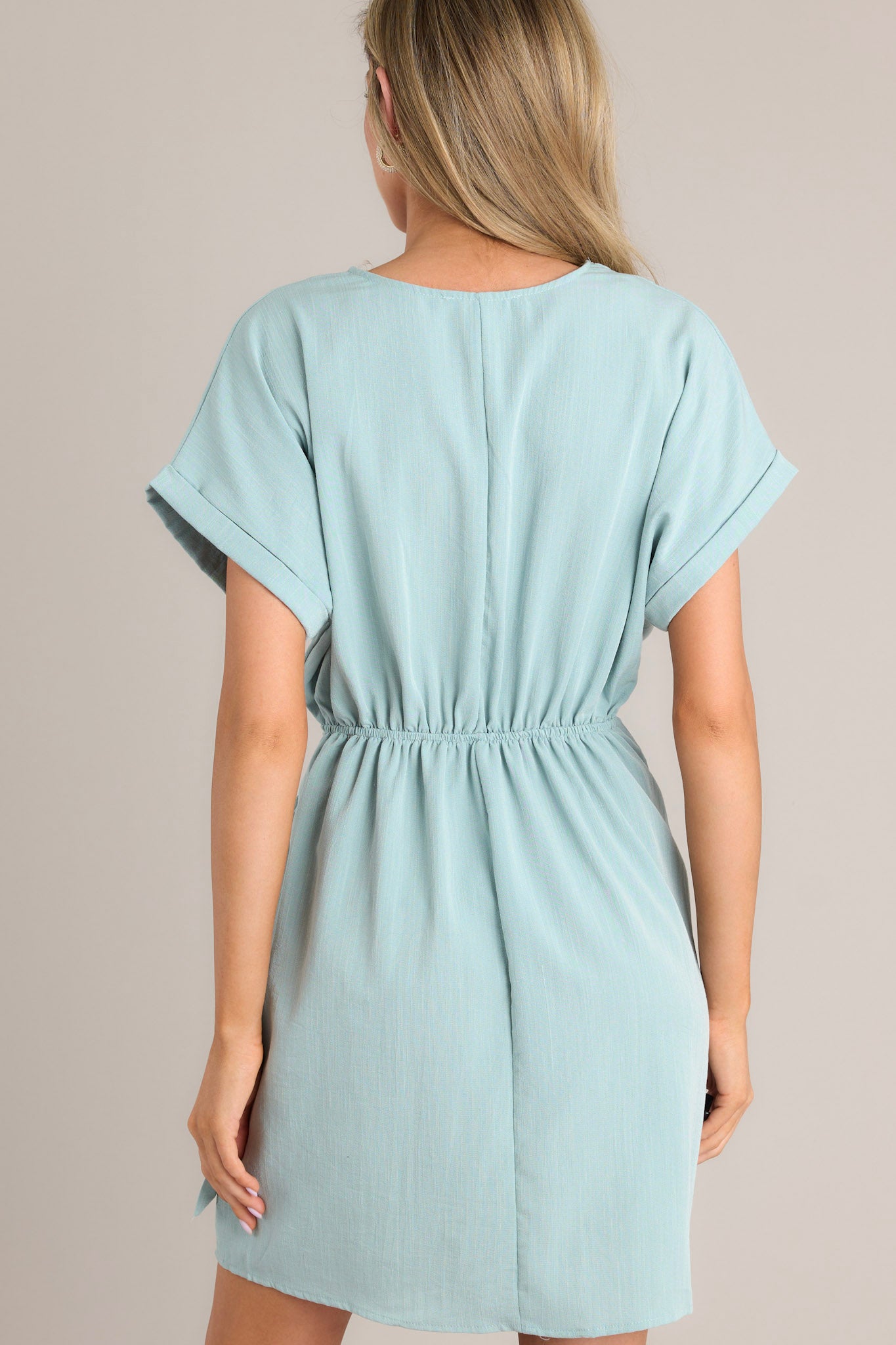 Back view of this dress that features a v-neckline, an elastic waist insert, a self-tie wrap feature, and wide cuffed short sleeves.