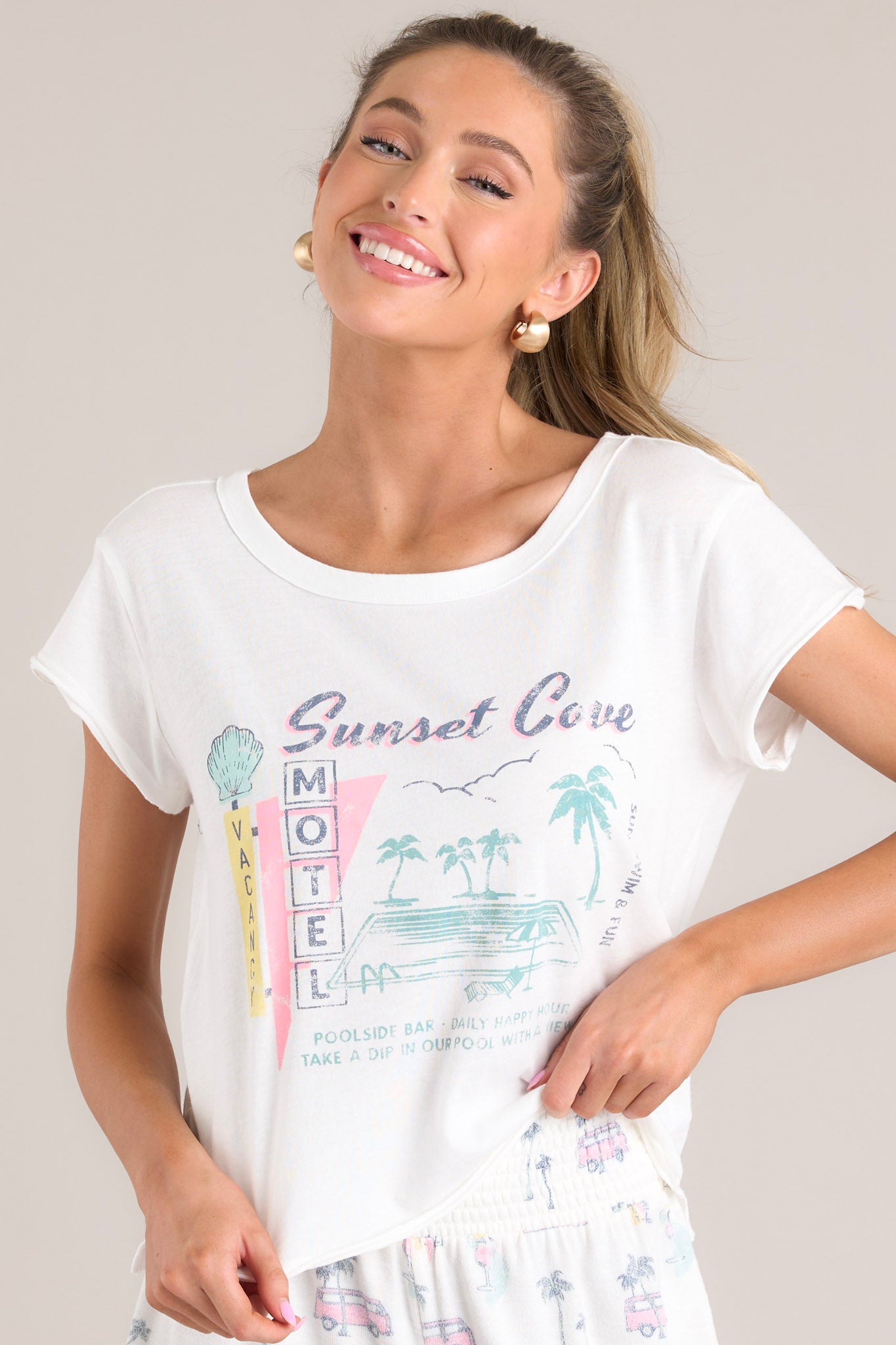 Front view of this tee that features a crew neckline, a vacation themed graphic, a light & airy material, a slightly cropped length, a split hemline, and short sleeves.