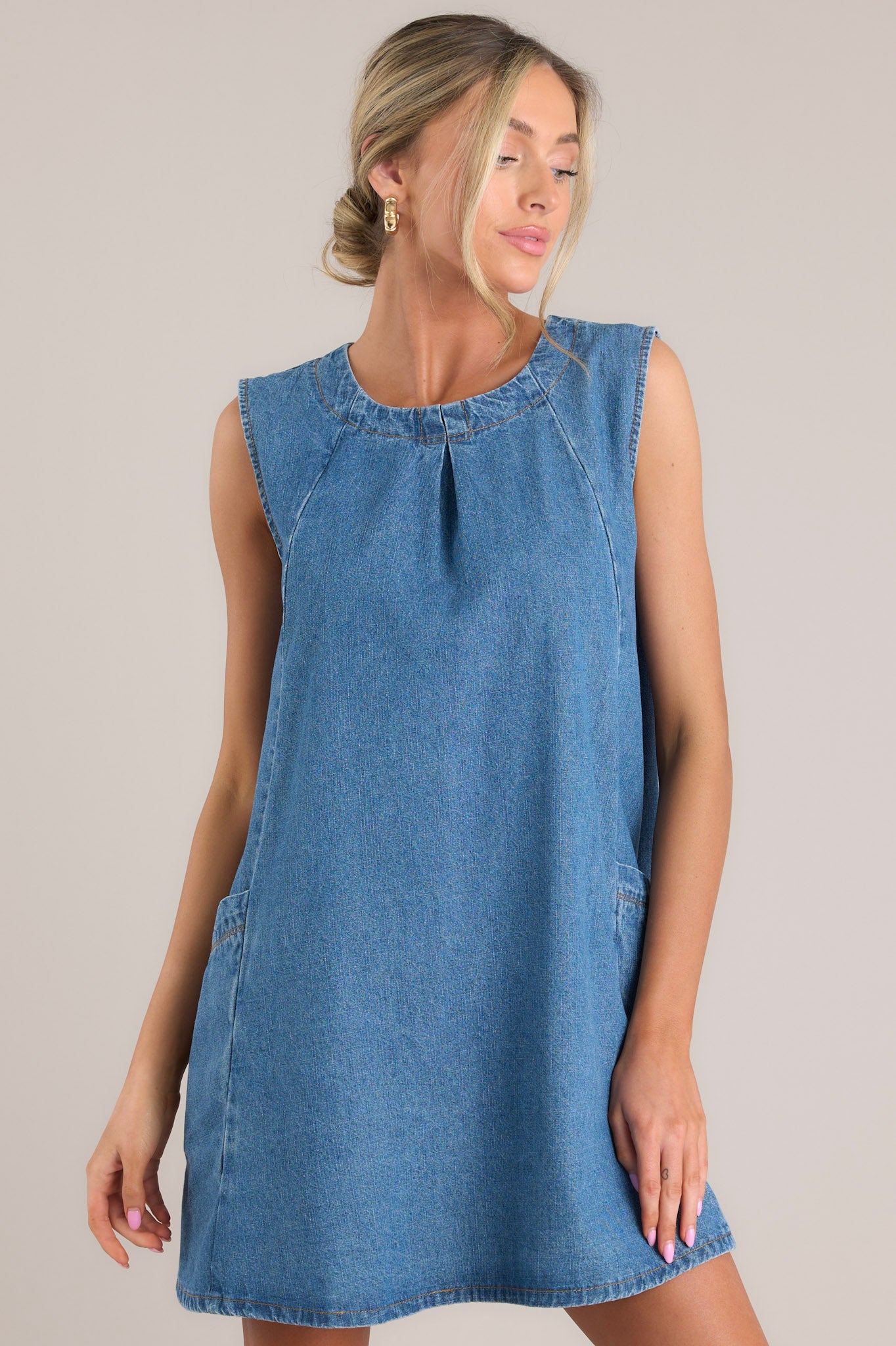 Front view of this dress that features a crew neckline, a double button clasp at the back, a single pleated detail at the center of the neckline, functional pockets at the hips, and a flowy skirt.