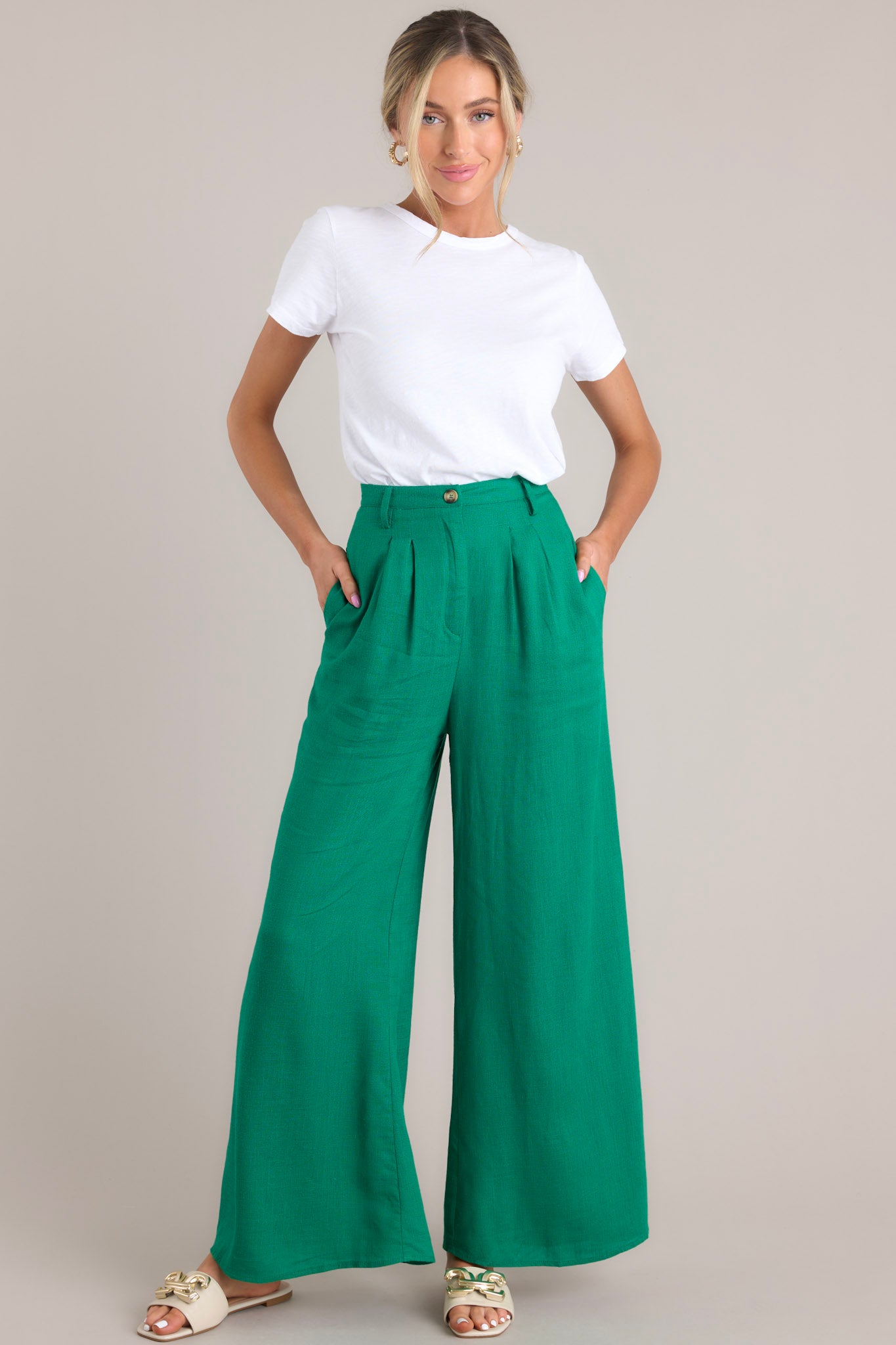 Full body view of these pants that feature a high waisted design, a functional button and zipper closure, belt loops, an elastic insert at the back of the waist, hip pockets, and a wide leg.