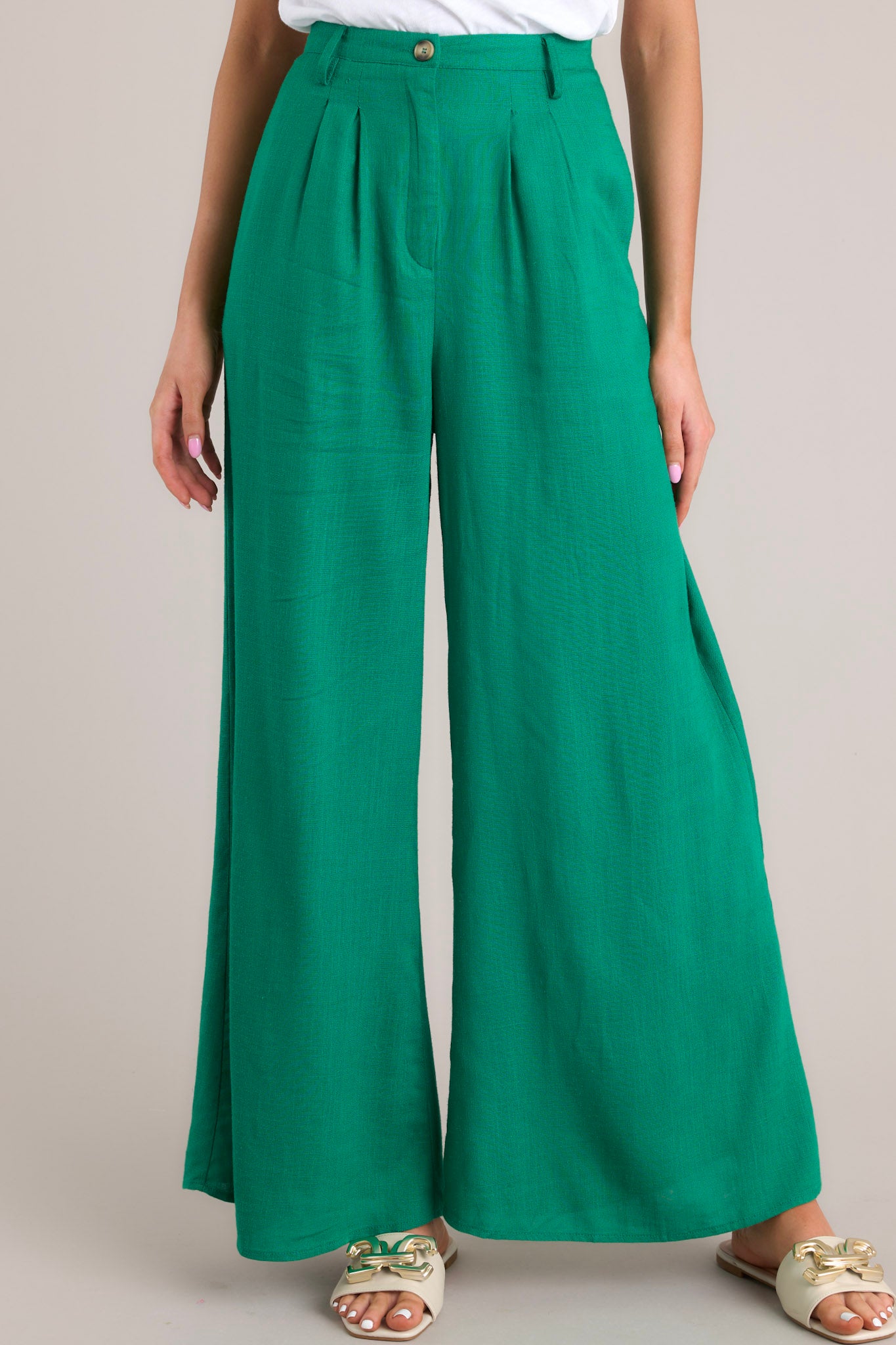 Front view of these pants that feature a high waisted design, a functional button and zipper closure, belt loops, an elastic insert at the back of the waist, hip pockets, and a wide leg.