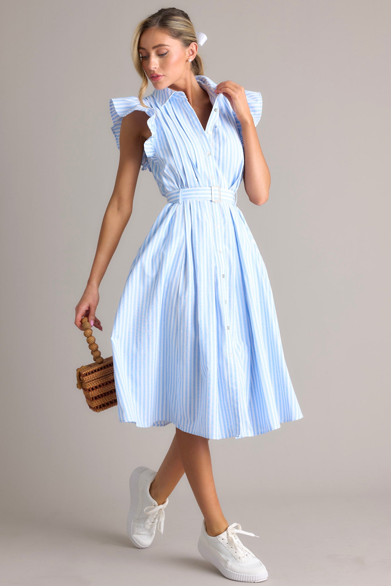 This blue dress features a collared neckline, ruffle sleeves, a full button front, pleated details throughout the front, belt loops, an adjustable belt with a functional buckle, and hip pockets.