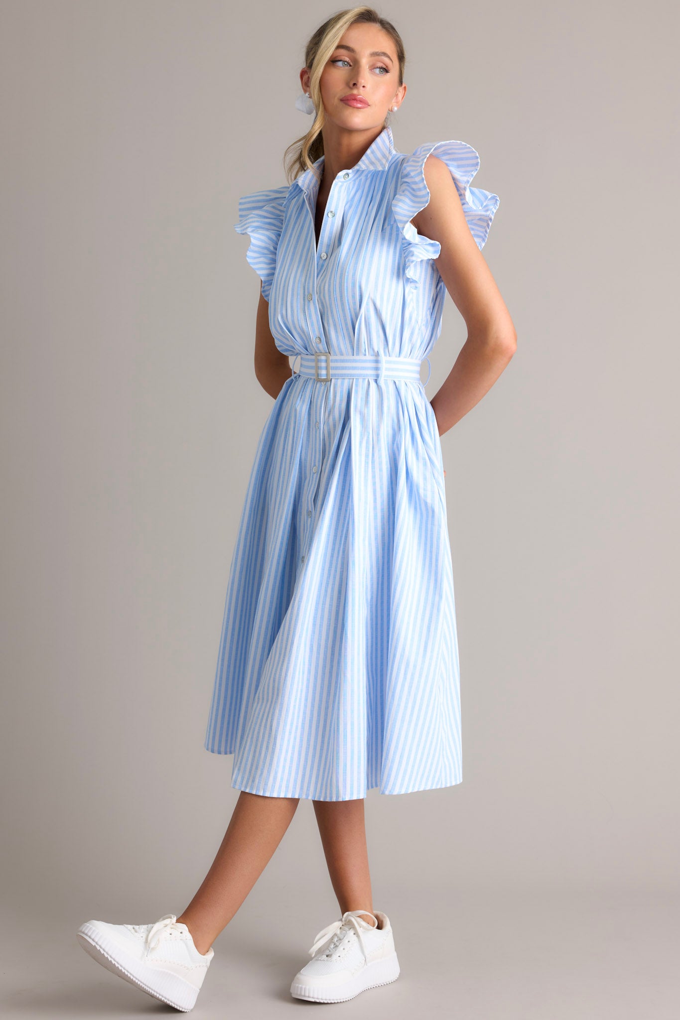 Angled full body view of this dress that features a collared neckline, ruffle sleeves, a full button front, pleated details throughout the front, belt loops, an adjustable belt with a functional buckle, and hip pockets.