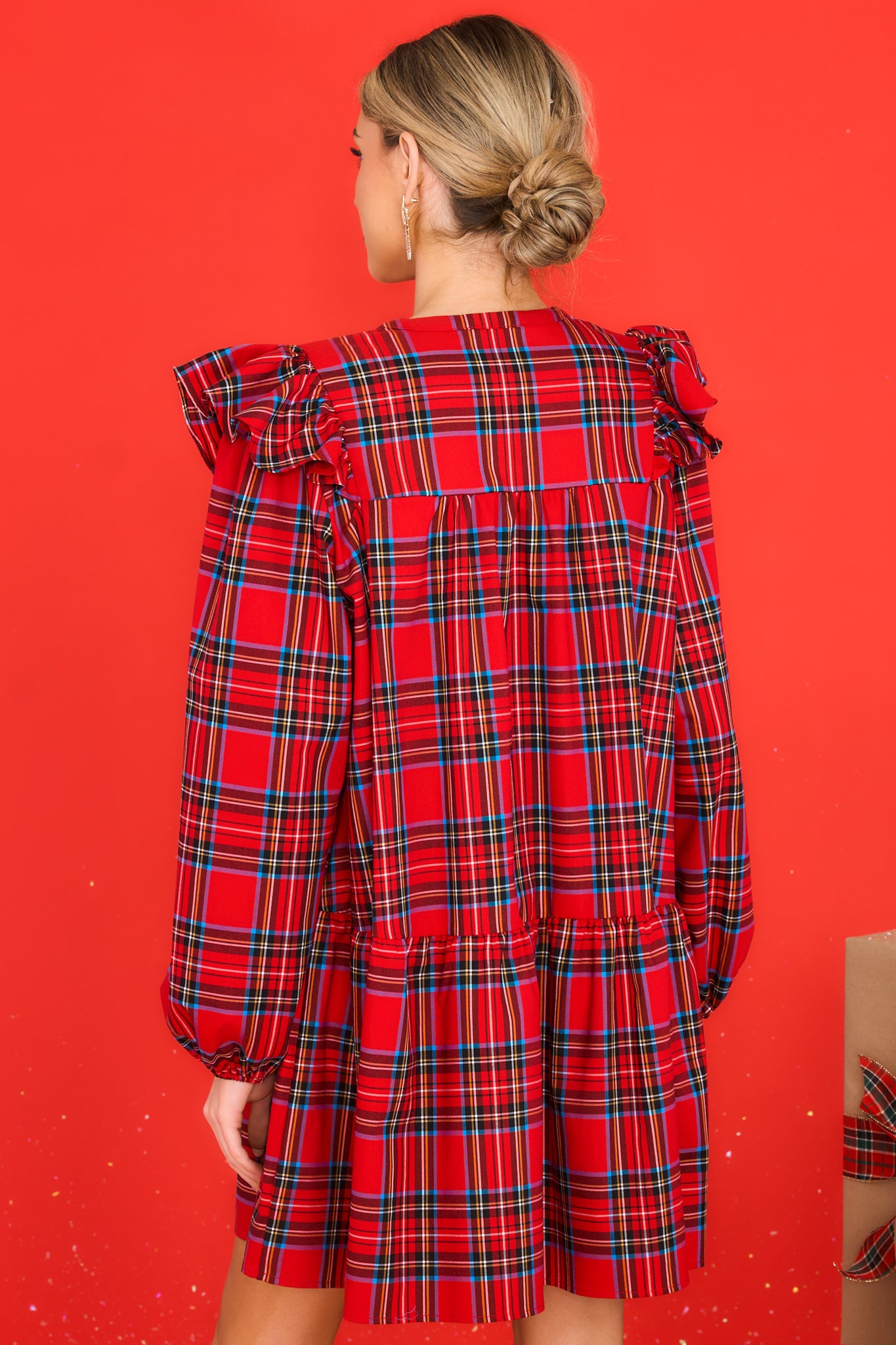 Back view of this dress that features a round neckline, three functional buttons down the front, ruffle detailing on the shoulders, long sleeves with elastic cuffs, and a babydoll silhouette.