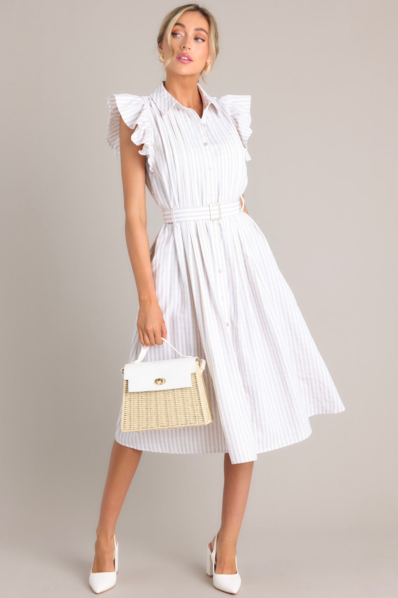 This white and tan dress features a collared neckline, ruffle sleeves, a full button front, pleated details throughout the front, belt loops, an adjustable belt with a functional buckle, and hip pockets.