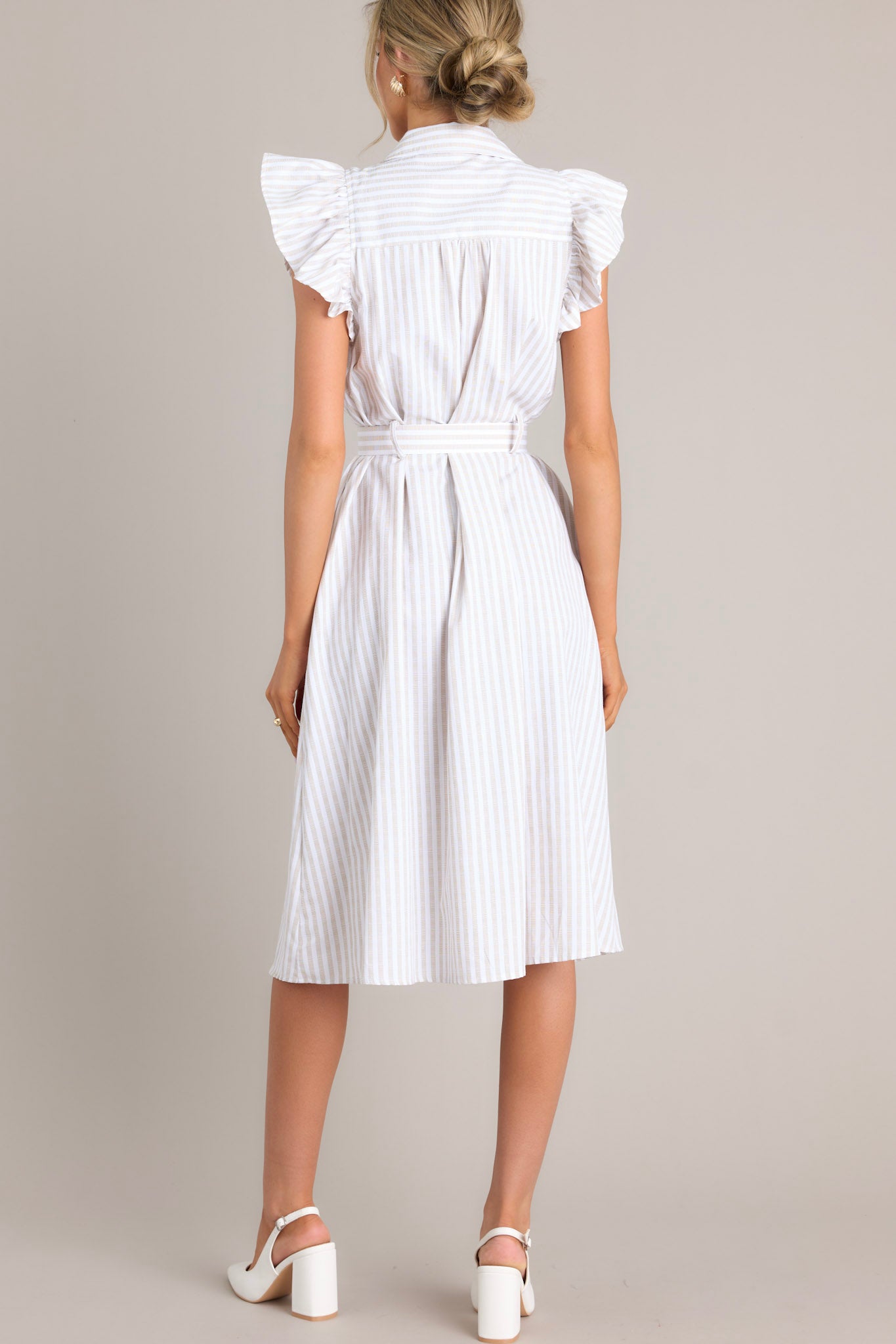 Back view of this dress that features a collared neckline, ruffle sleeves, a full button front, pleated details throughout the front, belt loops, an adjustable belt with a functional buckle, and hip pockets.